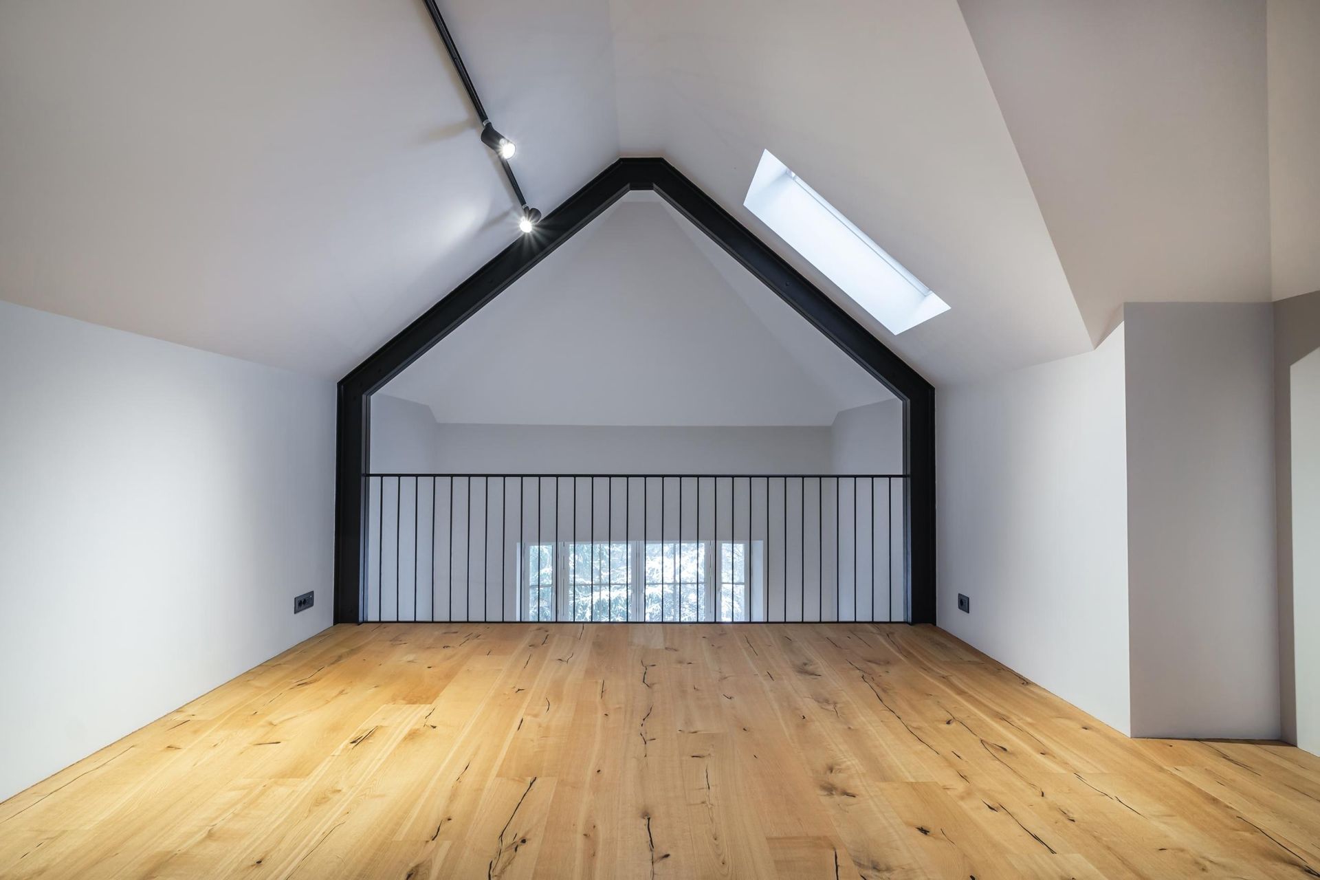 Loft space with wooden floor, black railing, and exposed beam; skylight overhead.