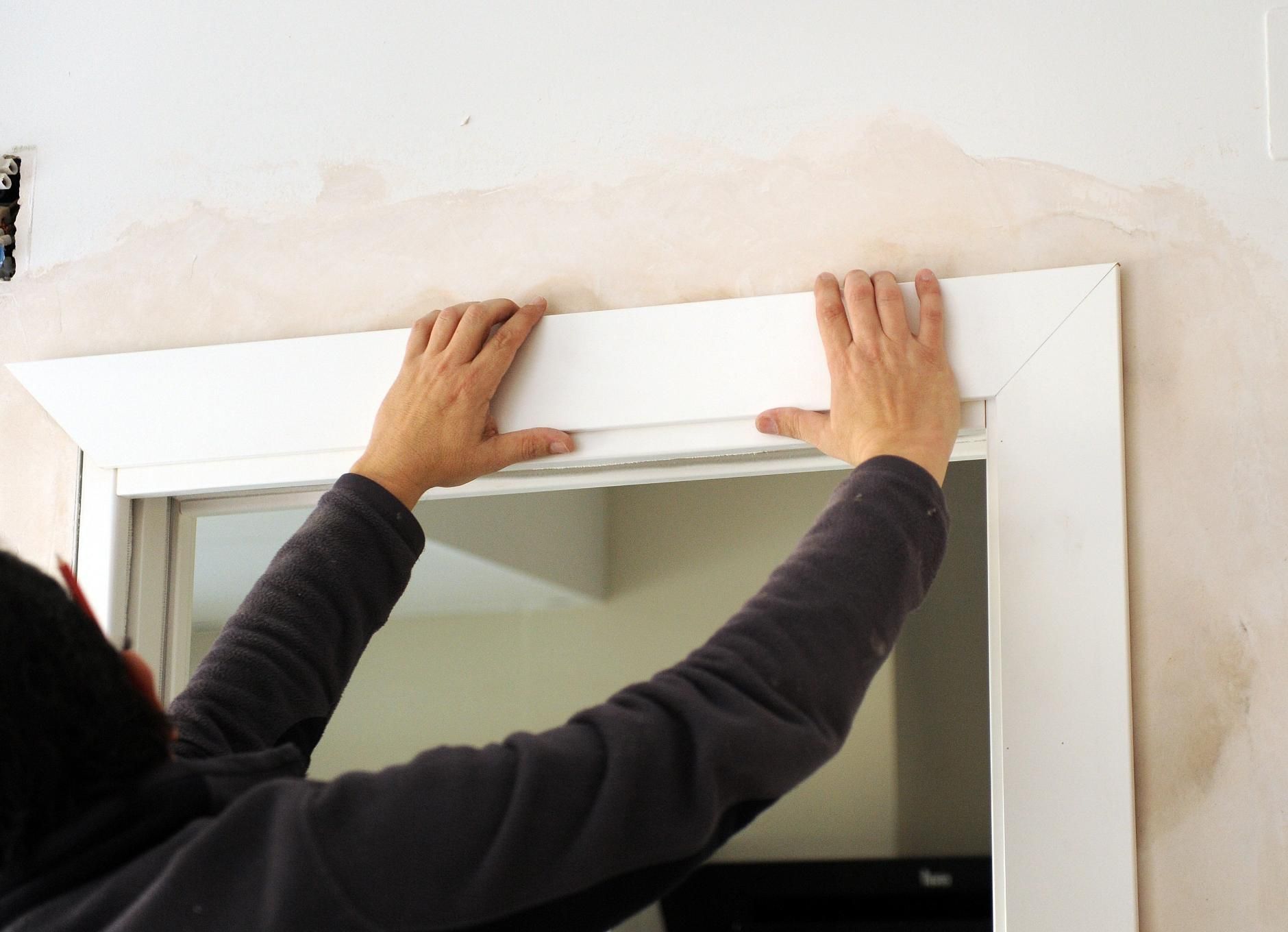 Person installing white door frame trim.