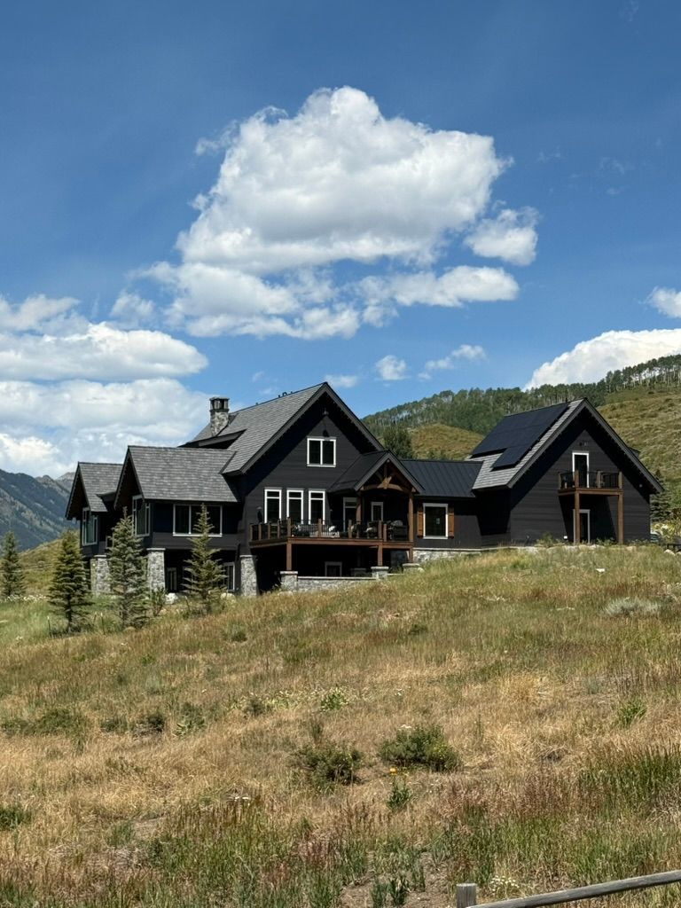 Dark house on a hillside under a blue sky with a puffy cloud.