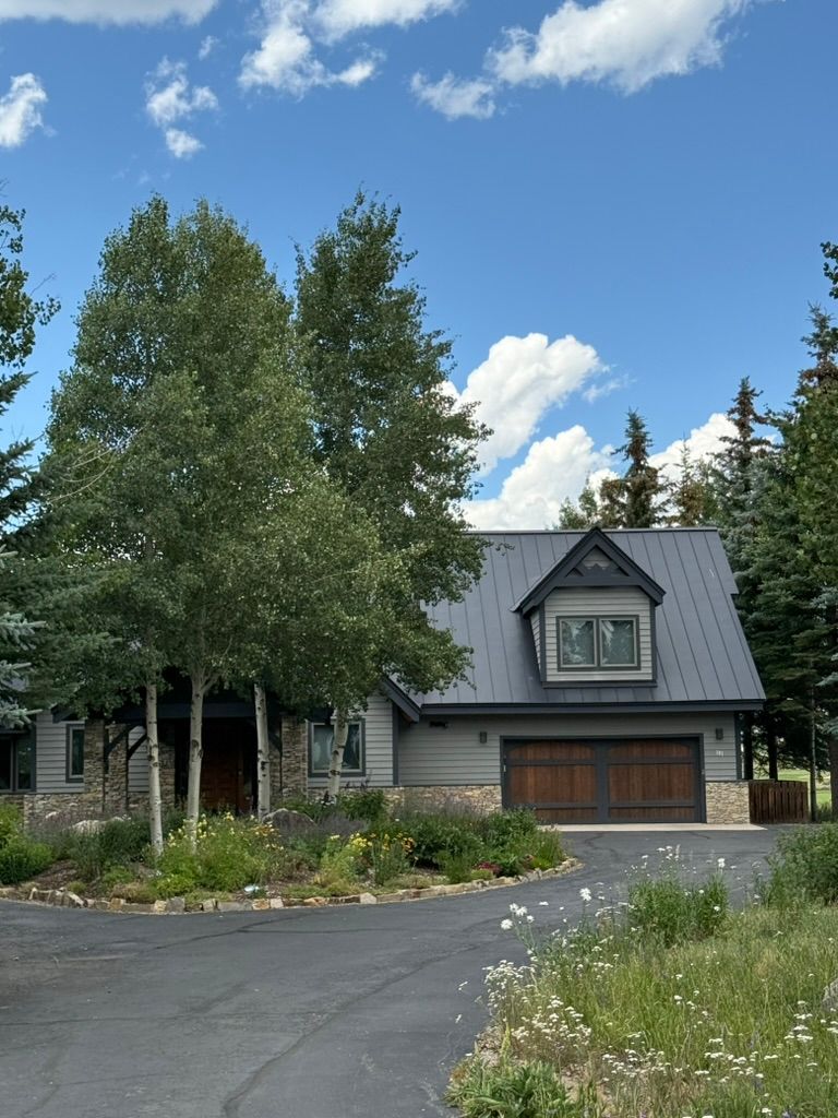 Gray house with brown garage doors and a dark roof, trees in front, blue sky.
