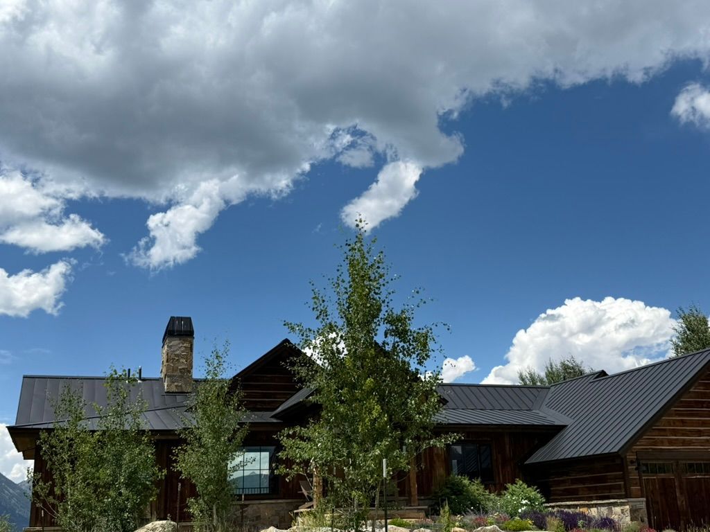 A rustic cabin with a dark roof under a bright blue sky filled with fluffy white clouds.