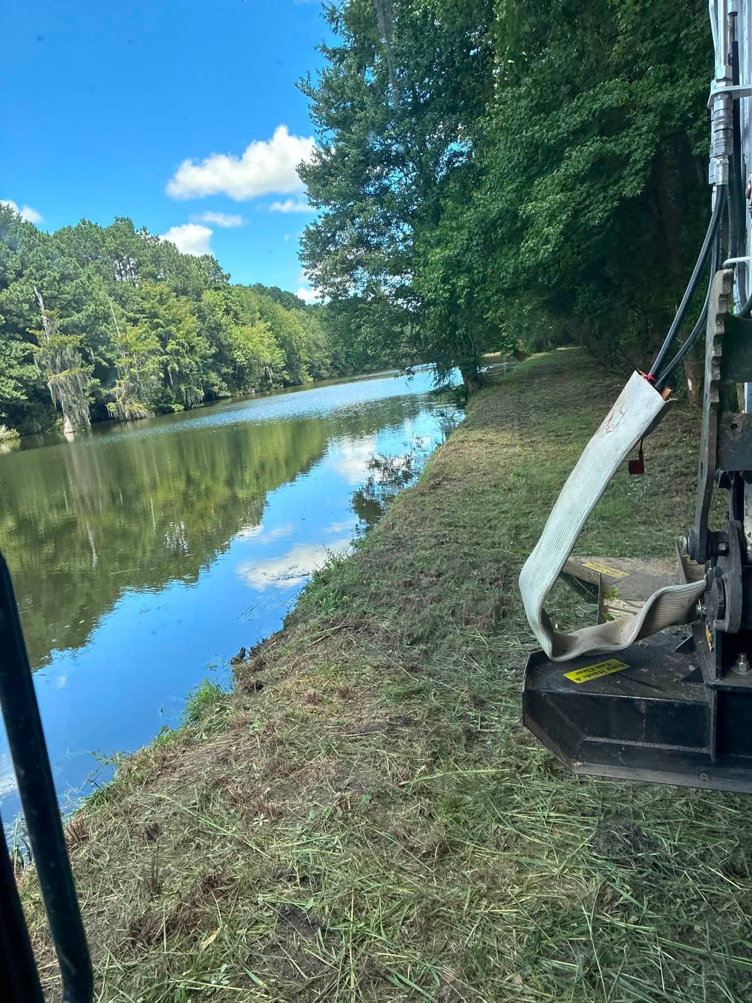 Canal beside trees and grassy bank, with excavator arm on the right and blue sky reflected in the water