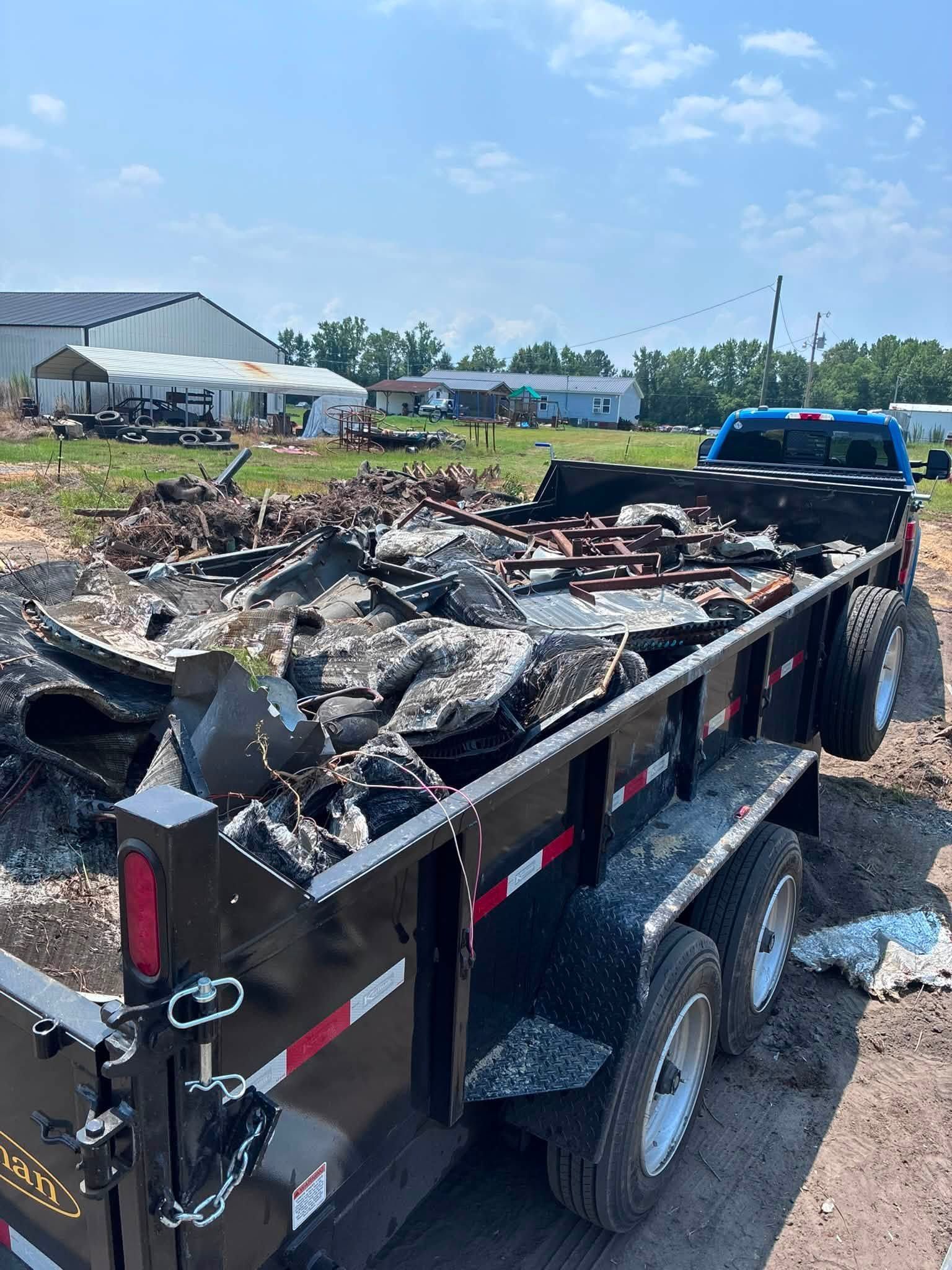 Charred debris in a trailer by a roadside, with a blue truck and houses in the background.