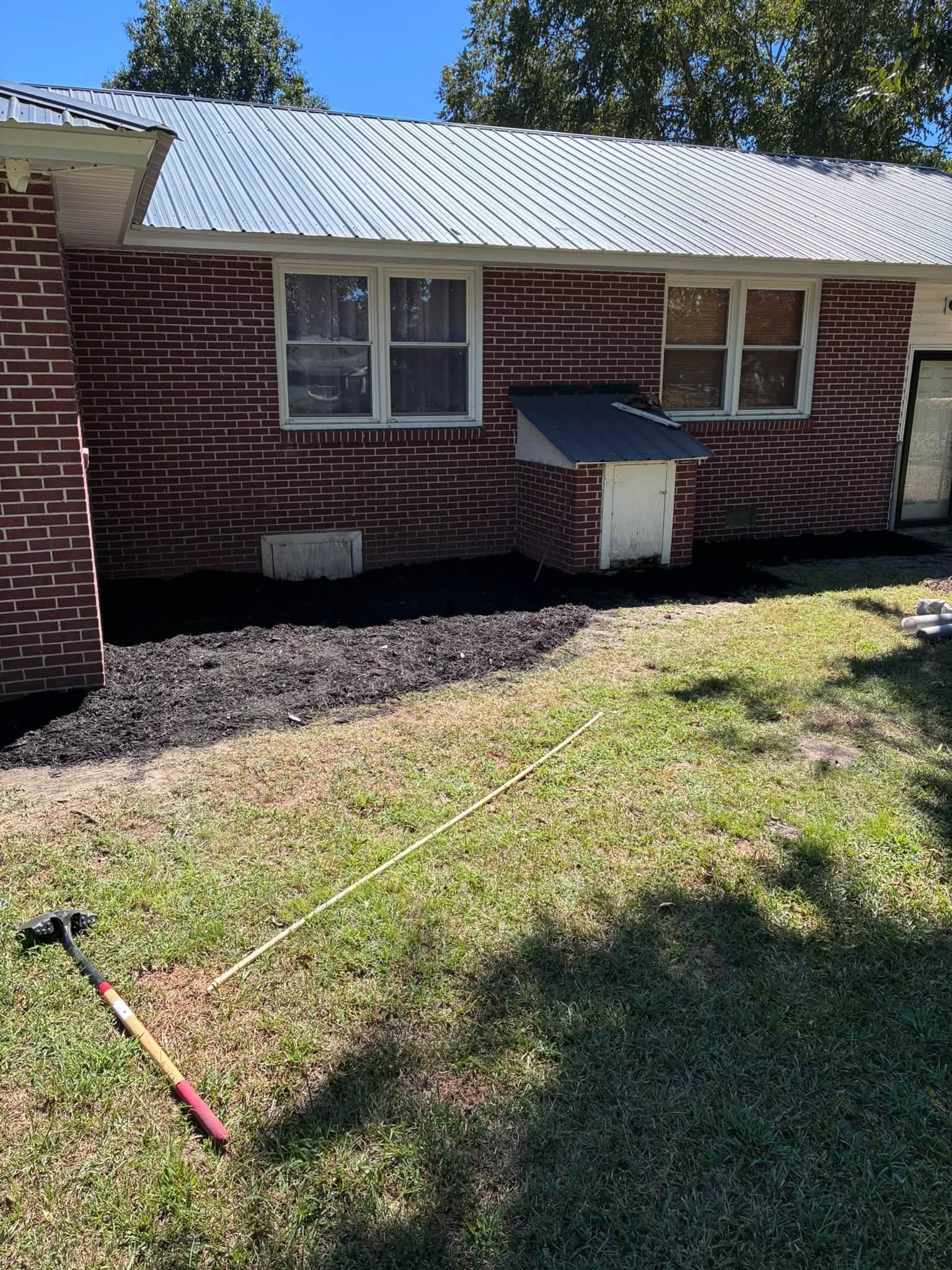 Brick house exterior with white roof, two windows, and a small basement access door in a grassy yard