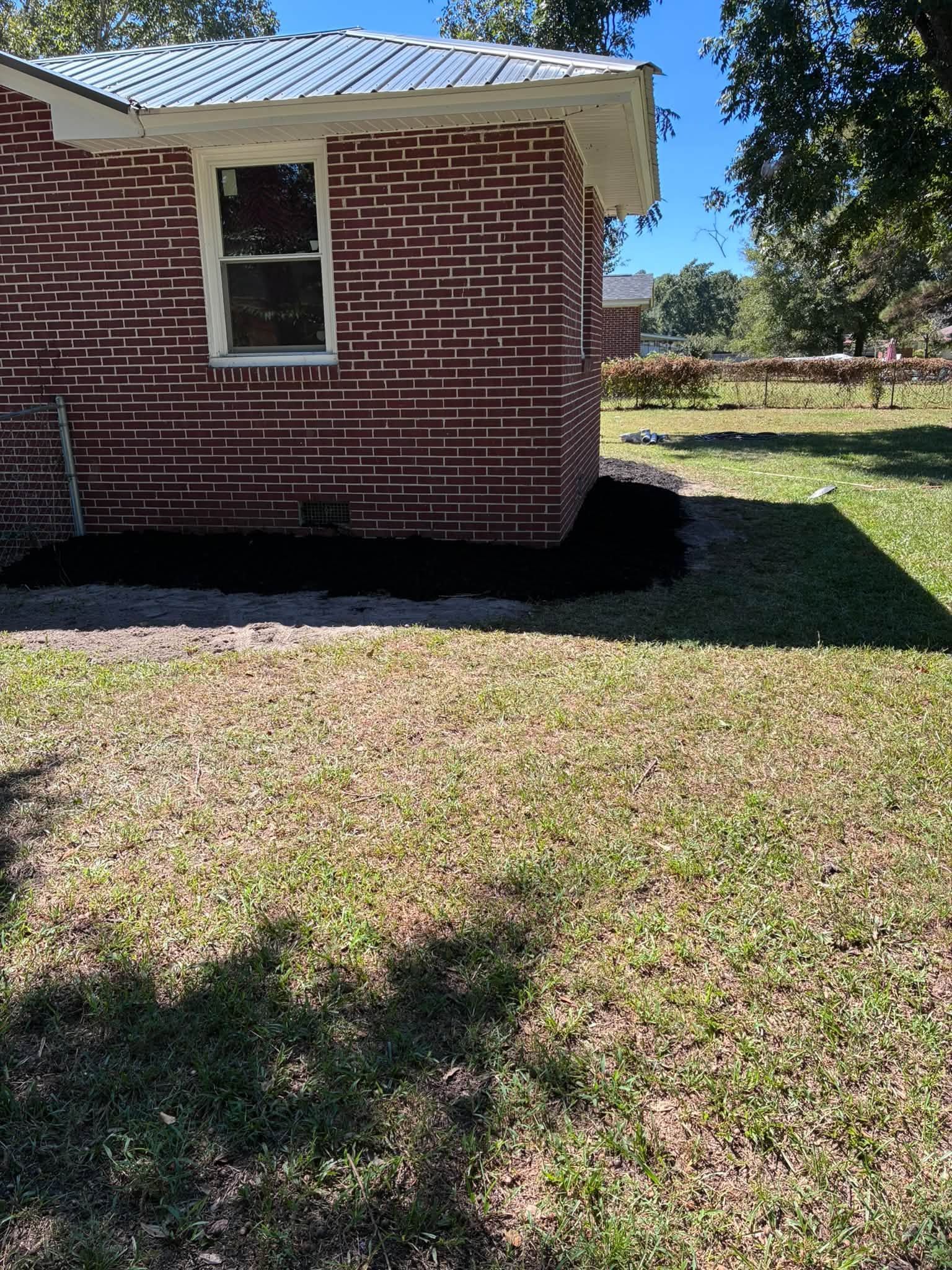 Brick house exterior with a white-trimmed window, grassy yard, and tree shadows in sunlight
