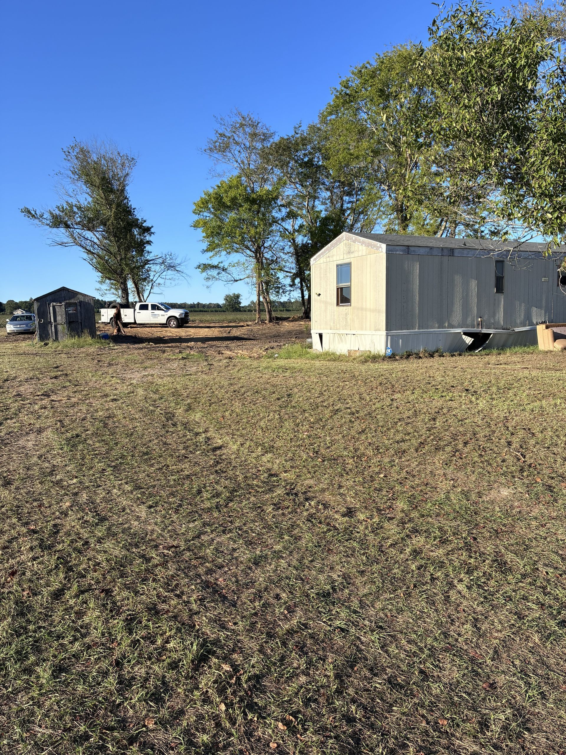 White mobile home in a grassy field with trees under a clear blue sky