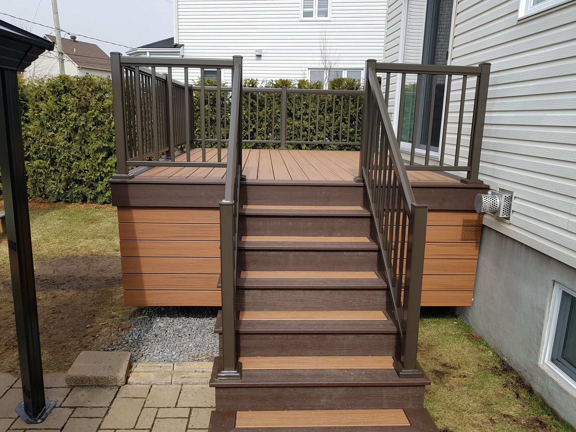 Terrasse surélevée en bois avec escalier et rambarde marron à côté d'une maison dans une cour arrière