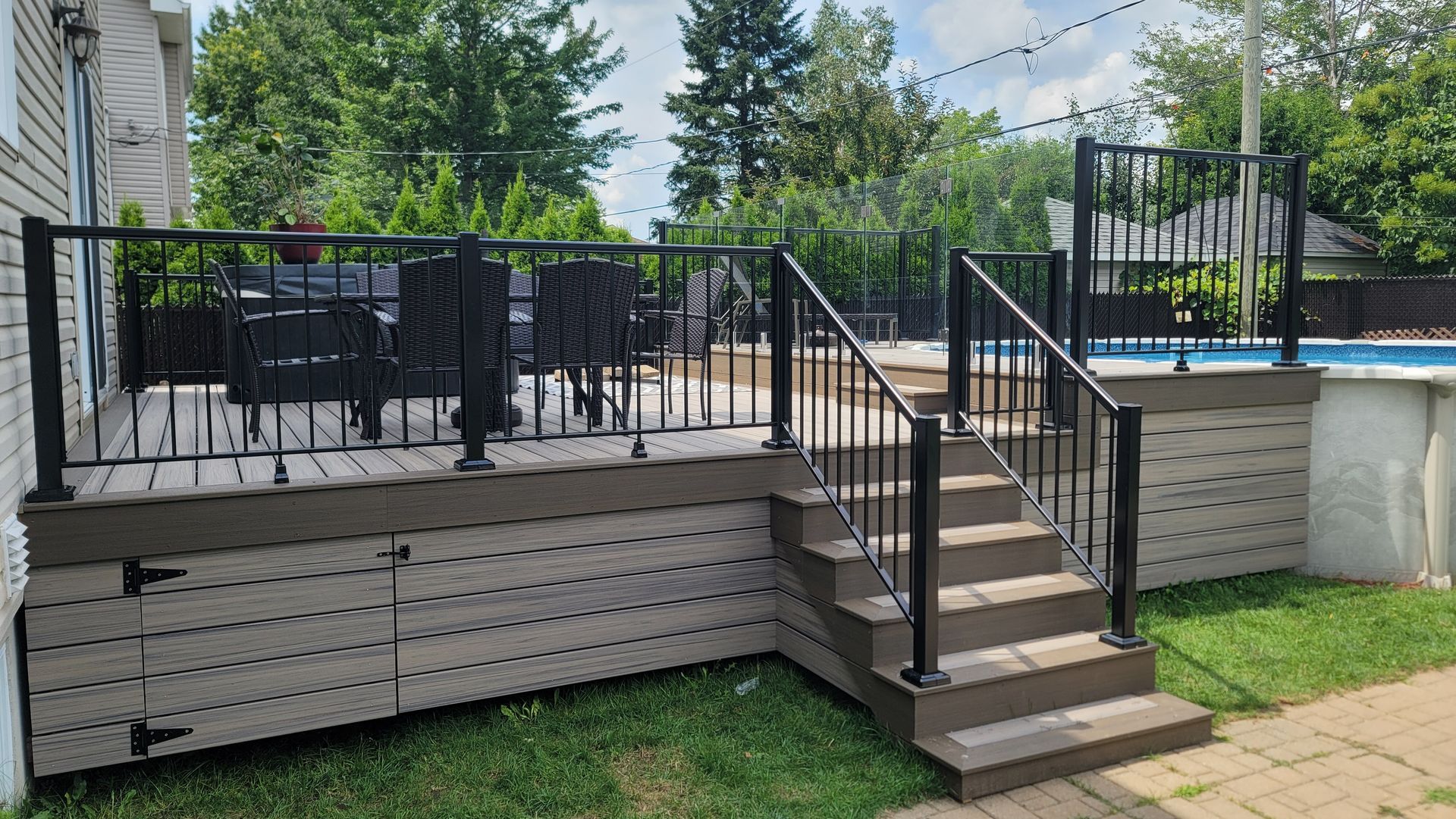 Terrasse arrière avec rambarde en métal noir, marches, mobilier de jardin et piscine hors sol à côté de la maison.