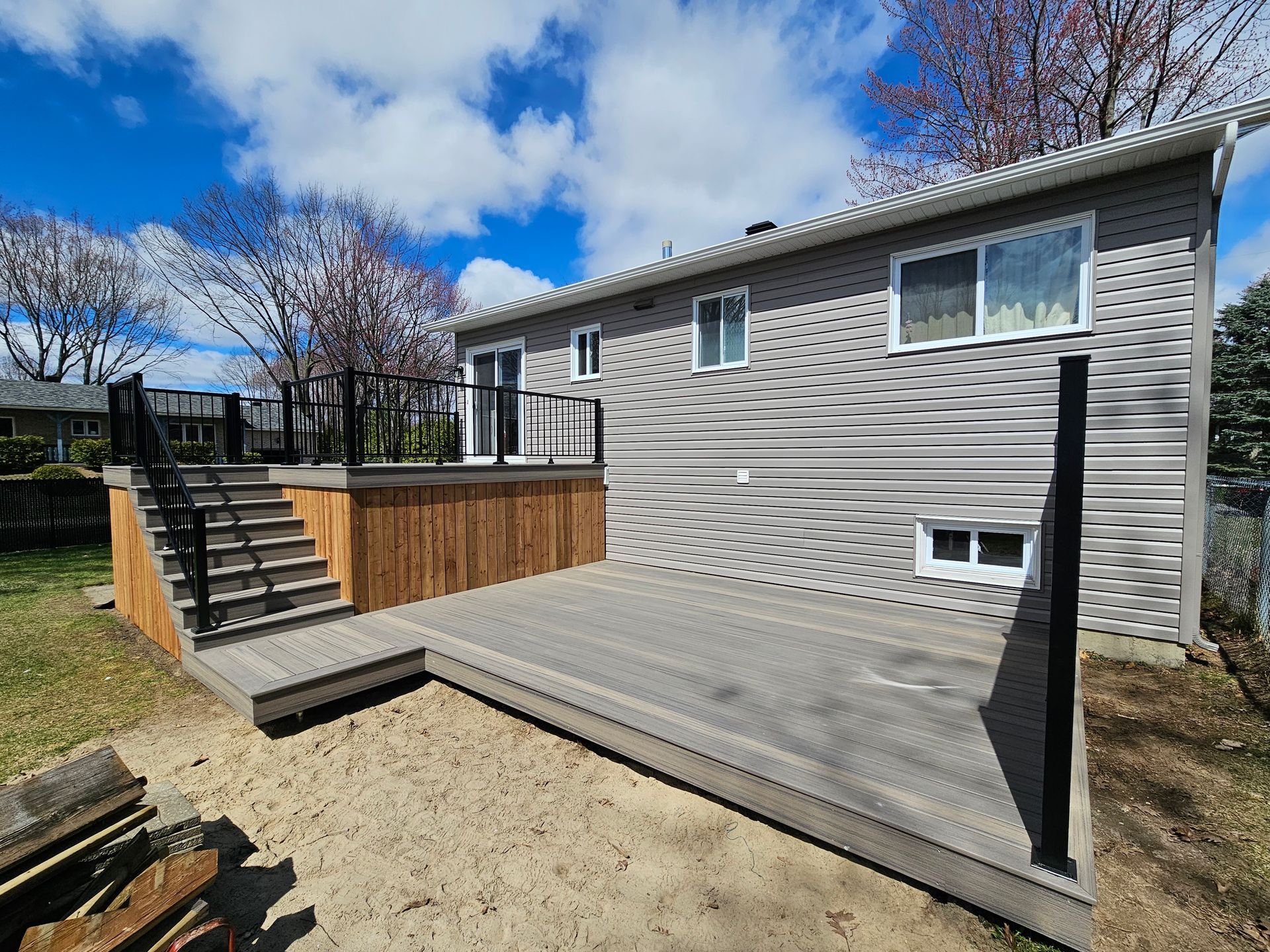 Terrasse en construction dans le jardin, à côté d'une maison grise, par une journée ensoleillée