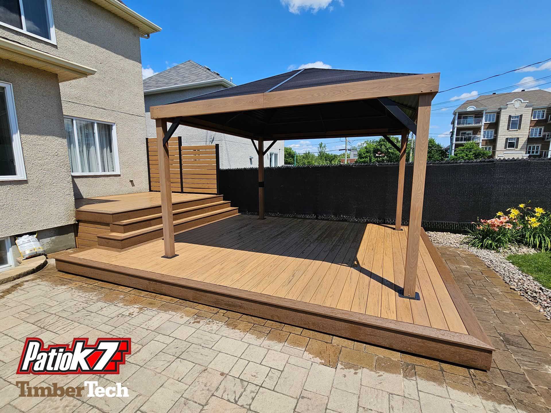 Terrasse arrière avec pergola en bois et marches jouxtant une maison en stuc, bordée de pavés et de fleurs