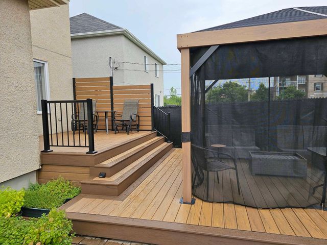 Terrasse arrière avec marches, rambarde noire, gazebo grillagé et allée en bois à côté d'une maison