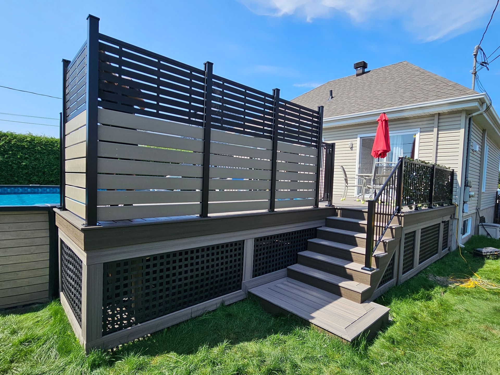 Terrasse arrière avec escalier, panneaux d'intimité gris et parasol rouge près d'une maison