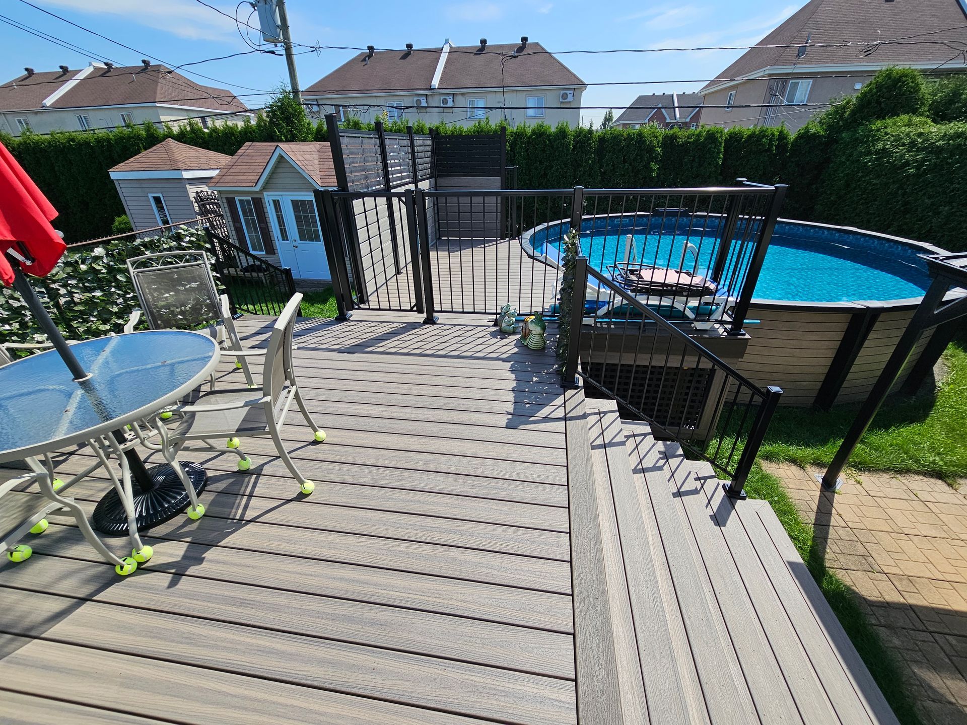 Terrasse arrière avec table de patio, rambarde, spa et piscine hors sol dans un jardin ensoleillé de banlieue