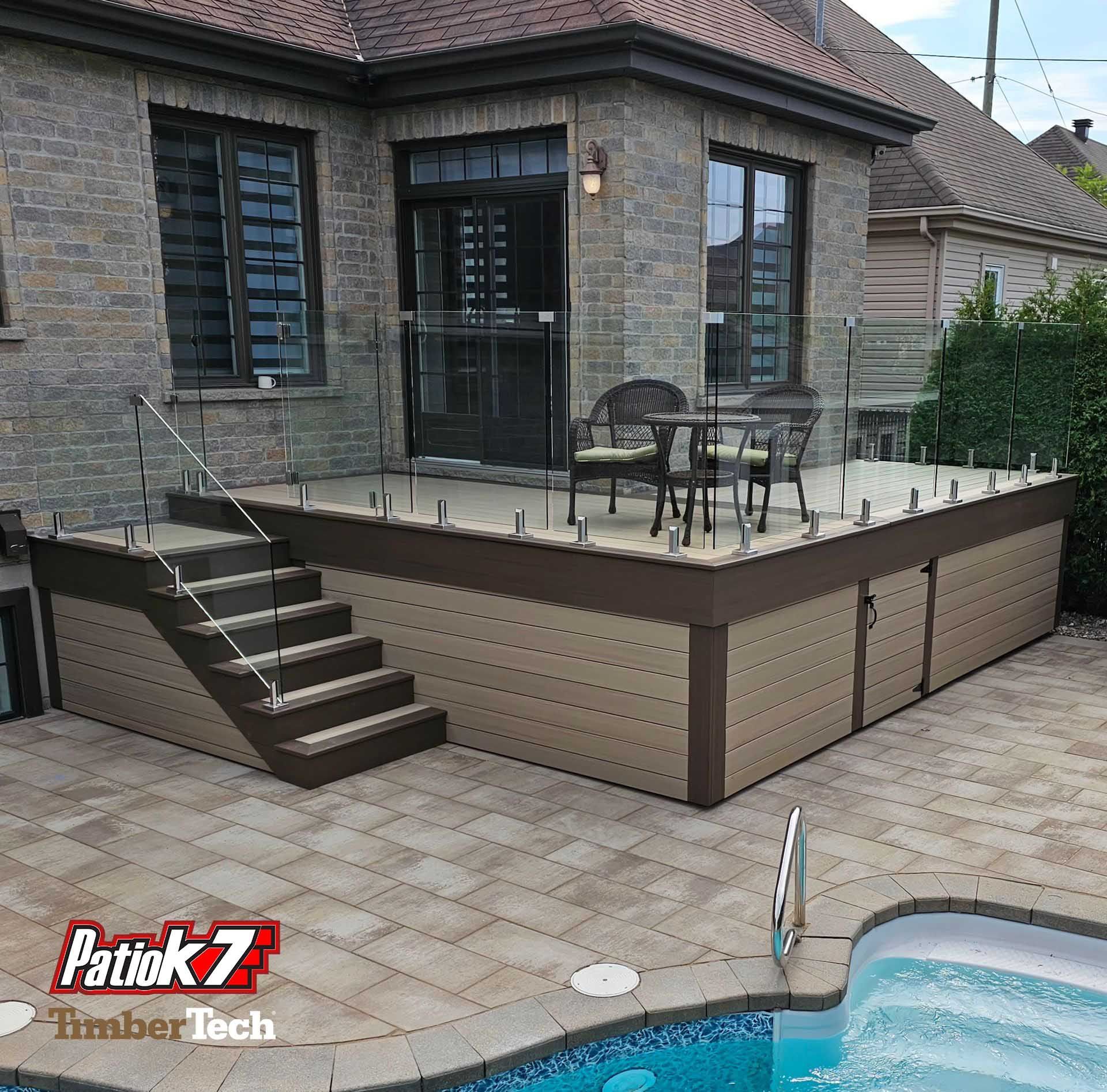 Terrasse surélevée attenante à une maison en briques, avec escalier, table et chaises, à côté d'une piscine.