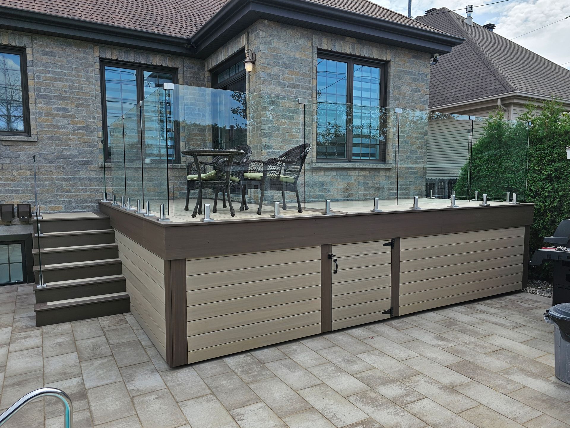 Terrasse avec table et chaises en métal jouxtant une maison en pierre, vue depuis une cour pavée.