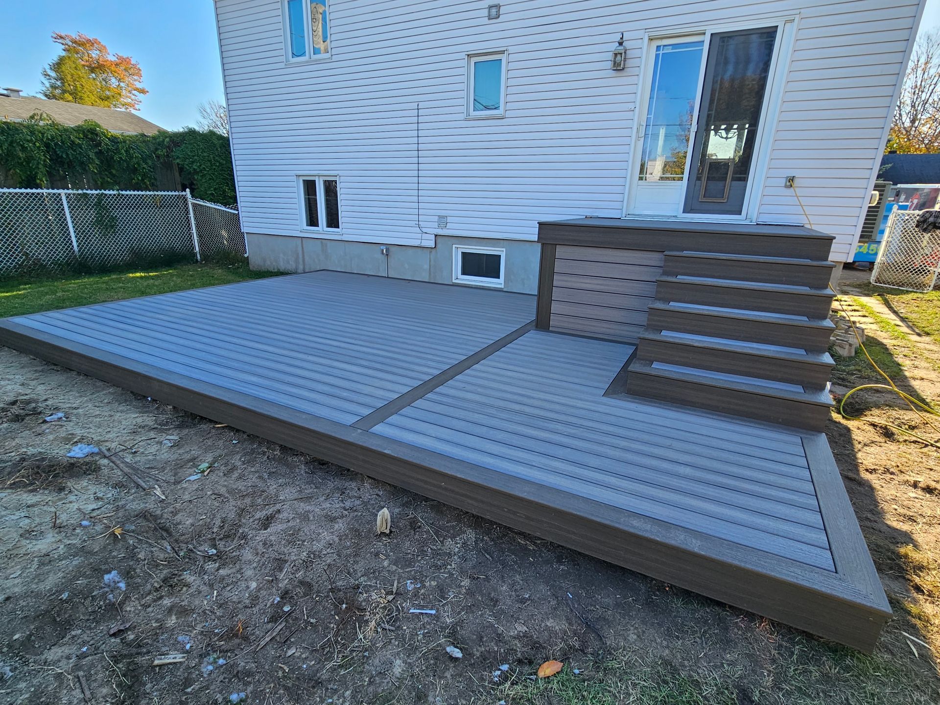 Terrasse arrière avec planches composites grises et marches en bois à côté d'une maison blanche