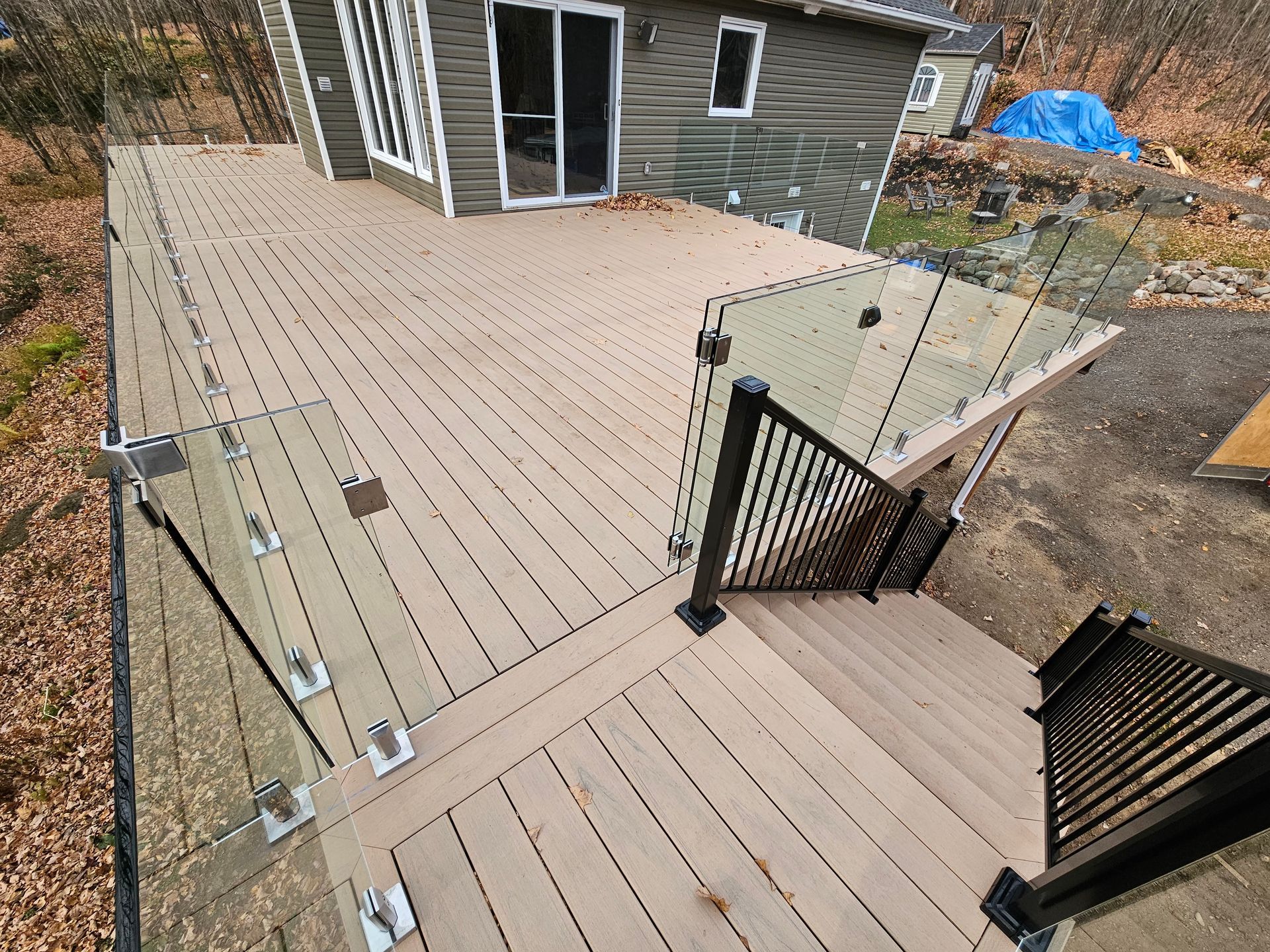 Terrasse en bois avec rambarde en verre et portail noir, vue d'en haut, à côté d'une maison.