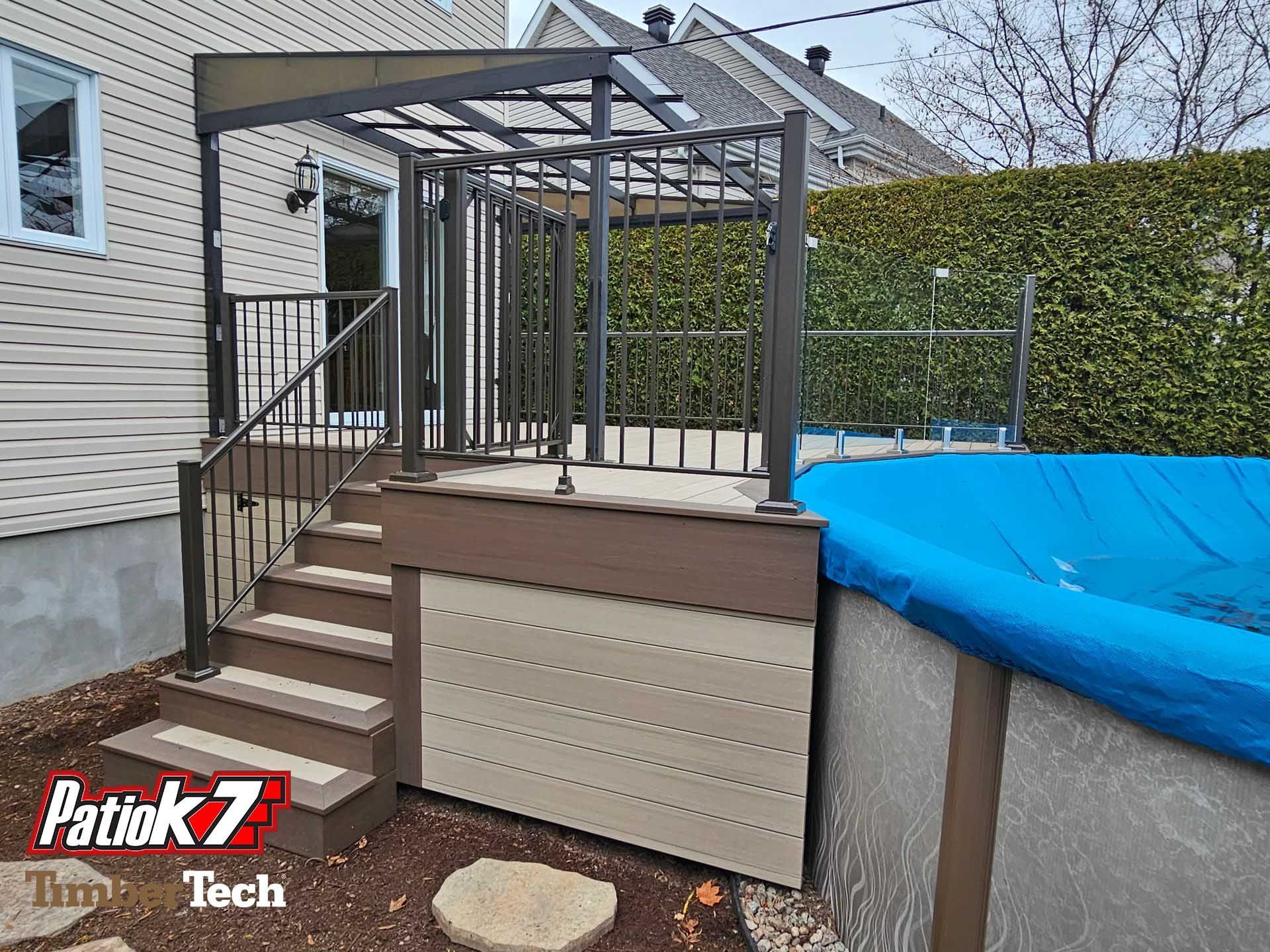 Escalier de terrasse arrière avec structure de pergola, bardage beige et piscine recouverte de bleu à côté d'une haie