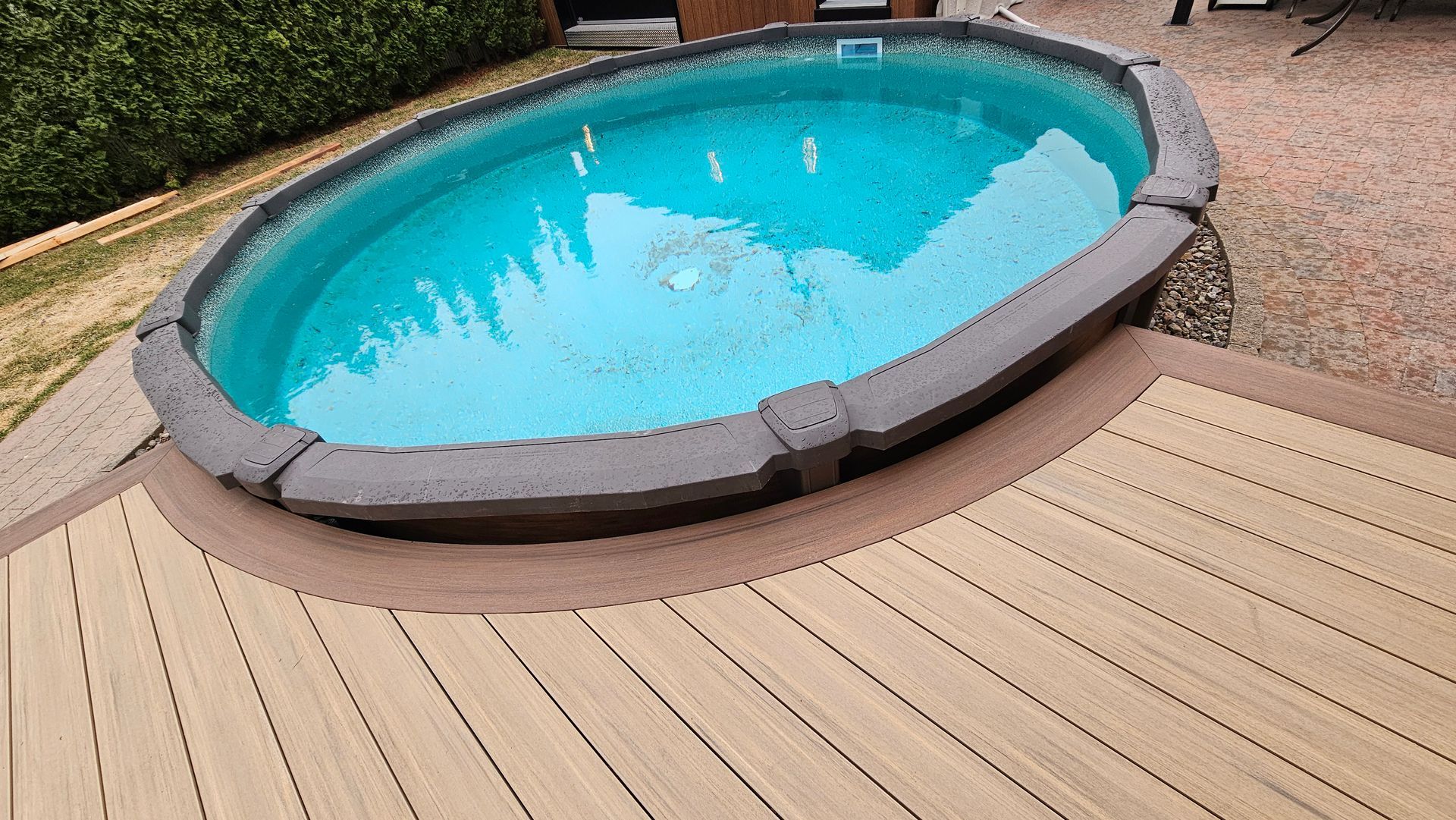 Petite piscine hors sol ovale aux eaux d'un bleu éclatant, jouxtant une terrasse en bois et un patio en gravier.