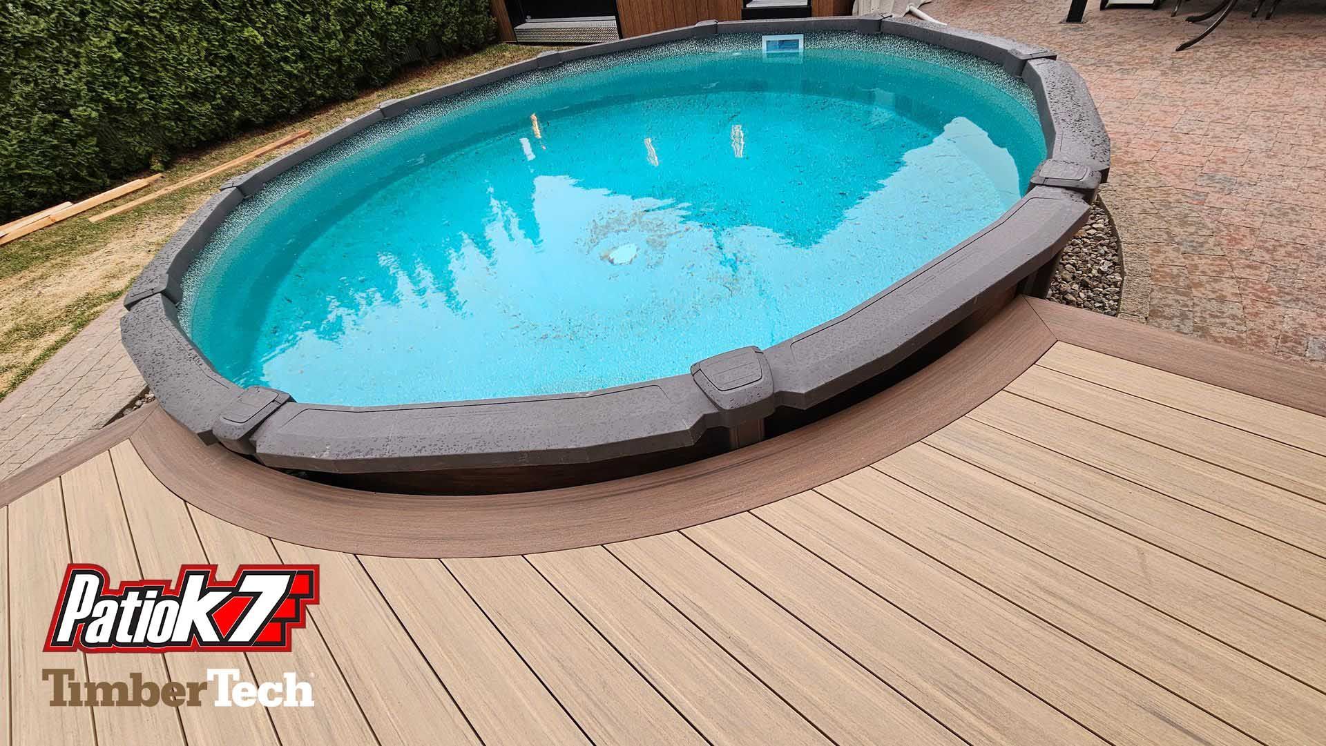 Piscine ovale dans le jardin avec une eau bleu vif, bordée d'une terrasse en bois clair.
