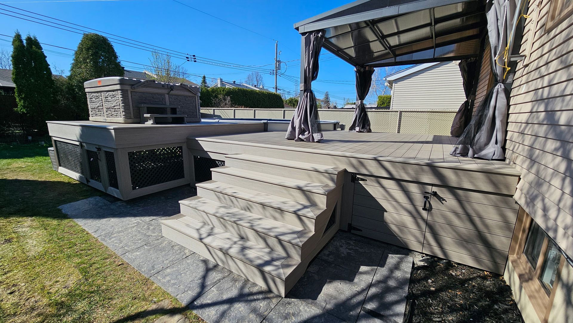 Terrasse arrière avec marches en pierre, terrasse surélevée et pergola couverte à côté d'un mur de briques.
