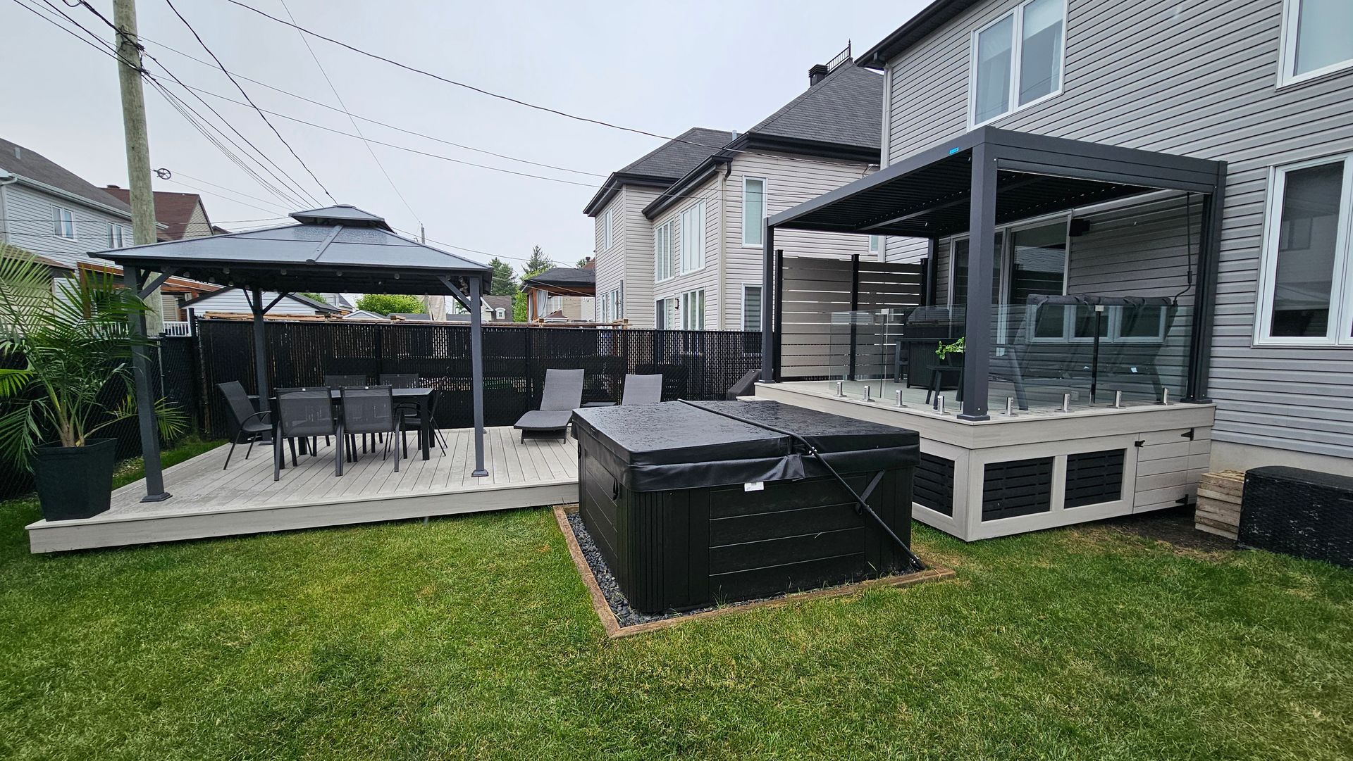 Terrasse arrière avec mobilier de jardin noir, un gazebo et une pelouse à côté d'une maison