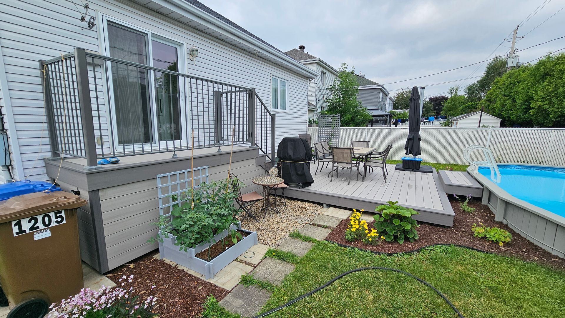 Terrasse arrière avec chaises longues, plantes en pot et barbecue à côté d'une piscine et de l'extérieur de la maison