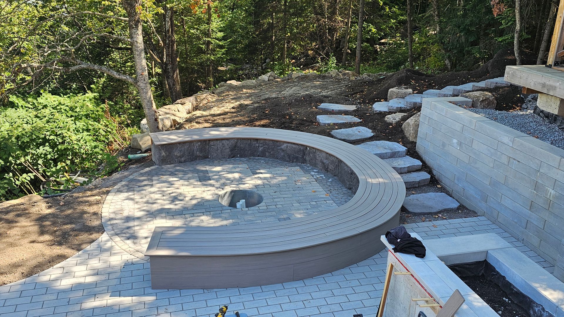 Construction d'une coque de spa en béton incurvée dans un jardin boisé, avec terrasse et maçonnerie apparentes.