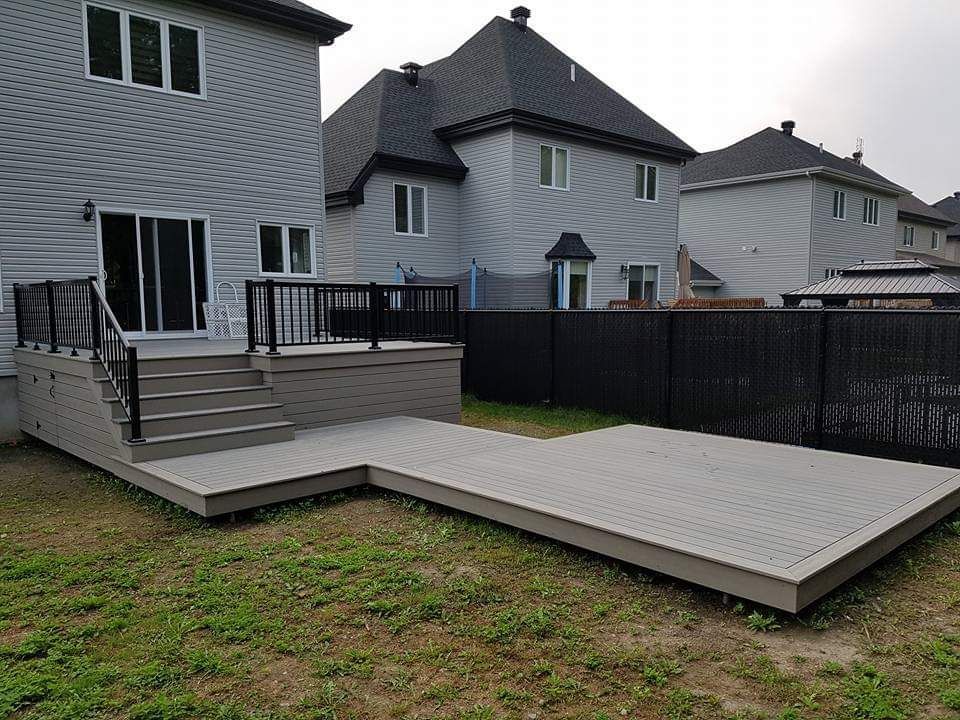 Terrasse en bois dans la cour arrière avec marches et grande plateforme basse à côté d'une maison et d'une cour clôturée