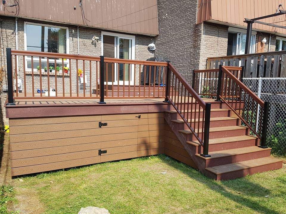 Escalier d'entrée et terrasse en bois sur la façade d'une maison de ville, avec un revêtement brun et une petite cour gazonnée.