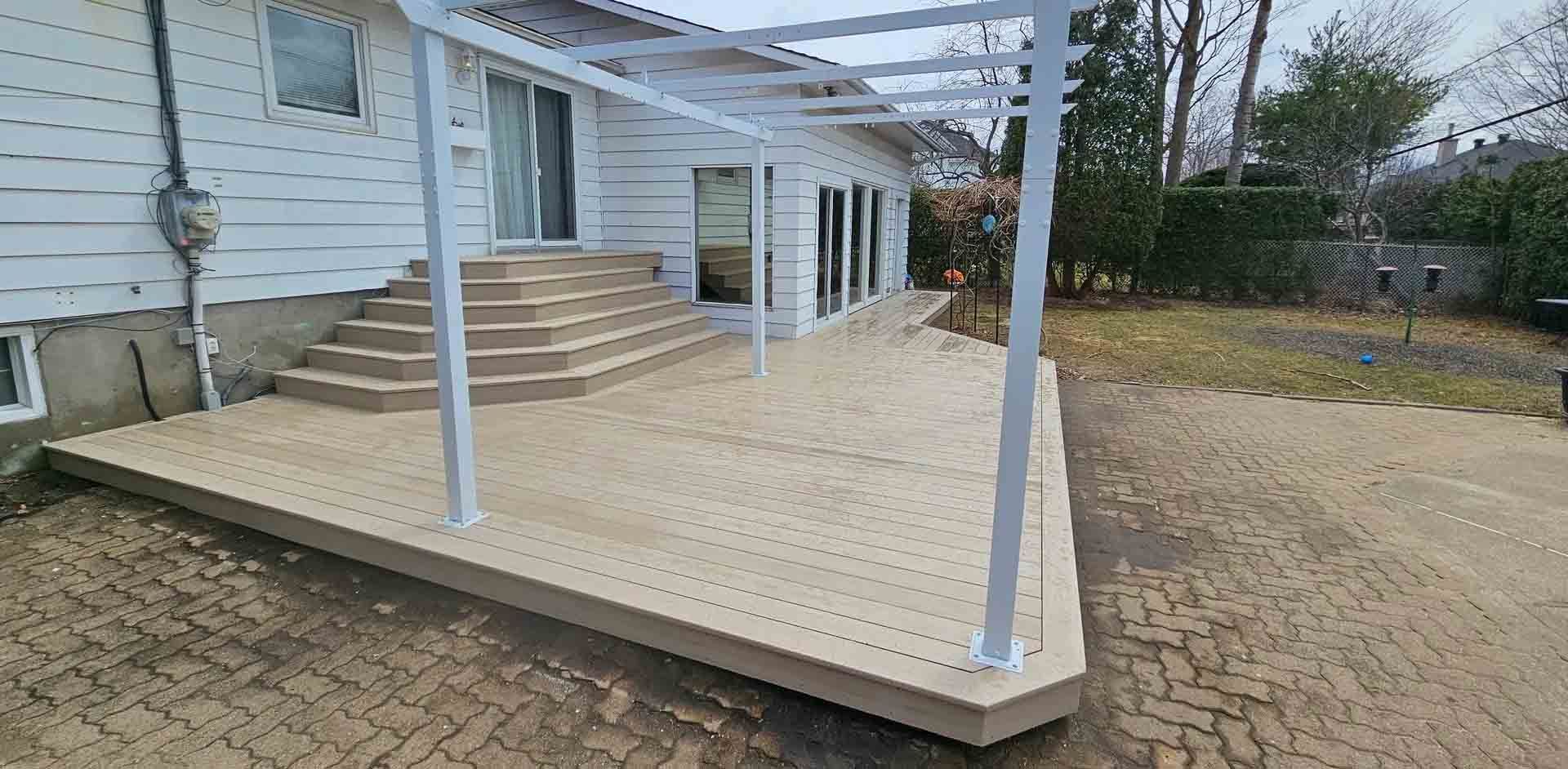 Rampe d'accès en bois couverte, avec escaliers et poteaux de soutien blancs, située à côté d'une maison blanche.