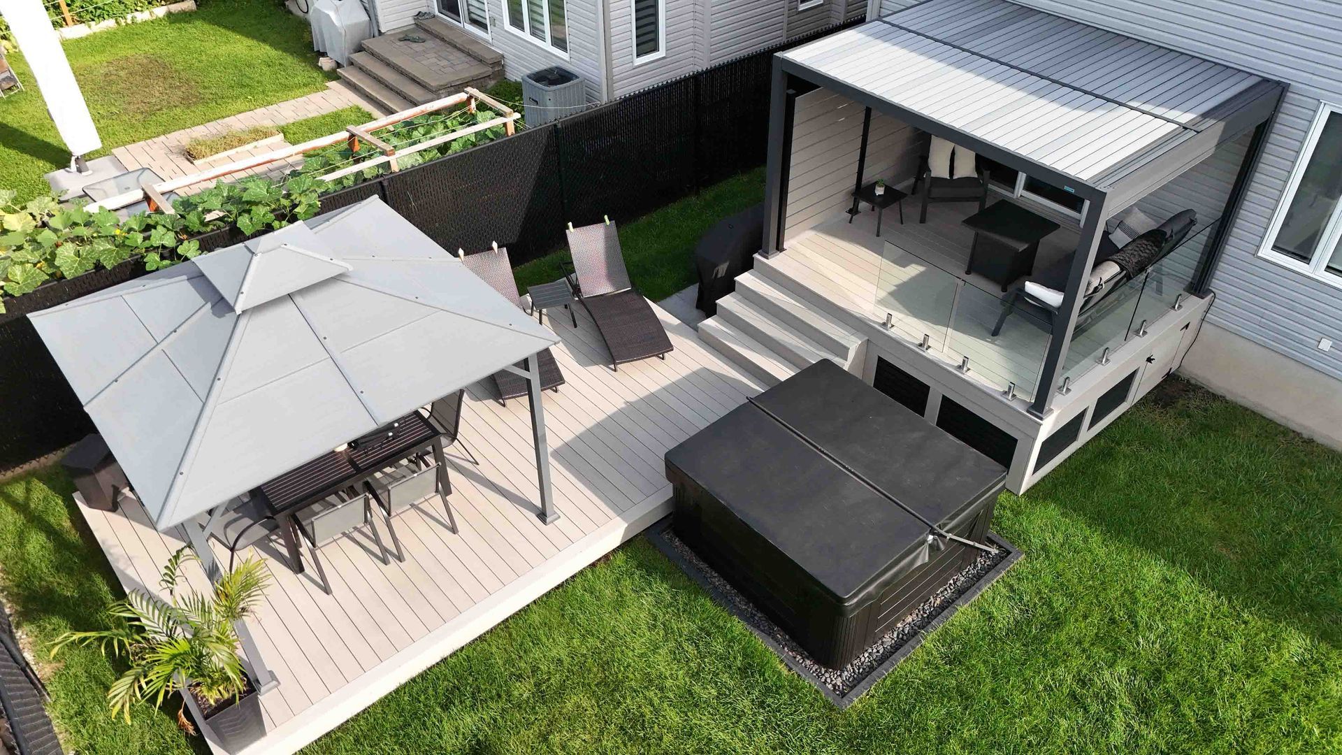 Terrasse avec rambarde noire, canapé d'angle bleu d'extérieur, table ronde et jacuzzi derrière une haie.