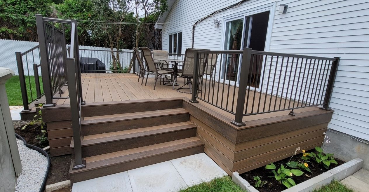 Terrasse arrière avec escalier marron, rambarde noire, plantes en pot et chaises de jardin