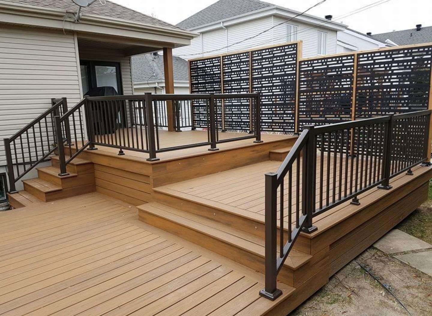 Terrasse surélevée en bois avec rambardes et escalier noirs, jouxtant une maison