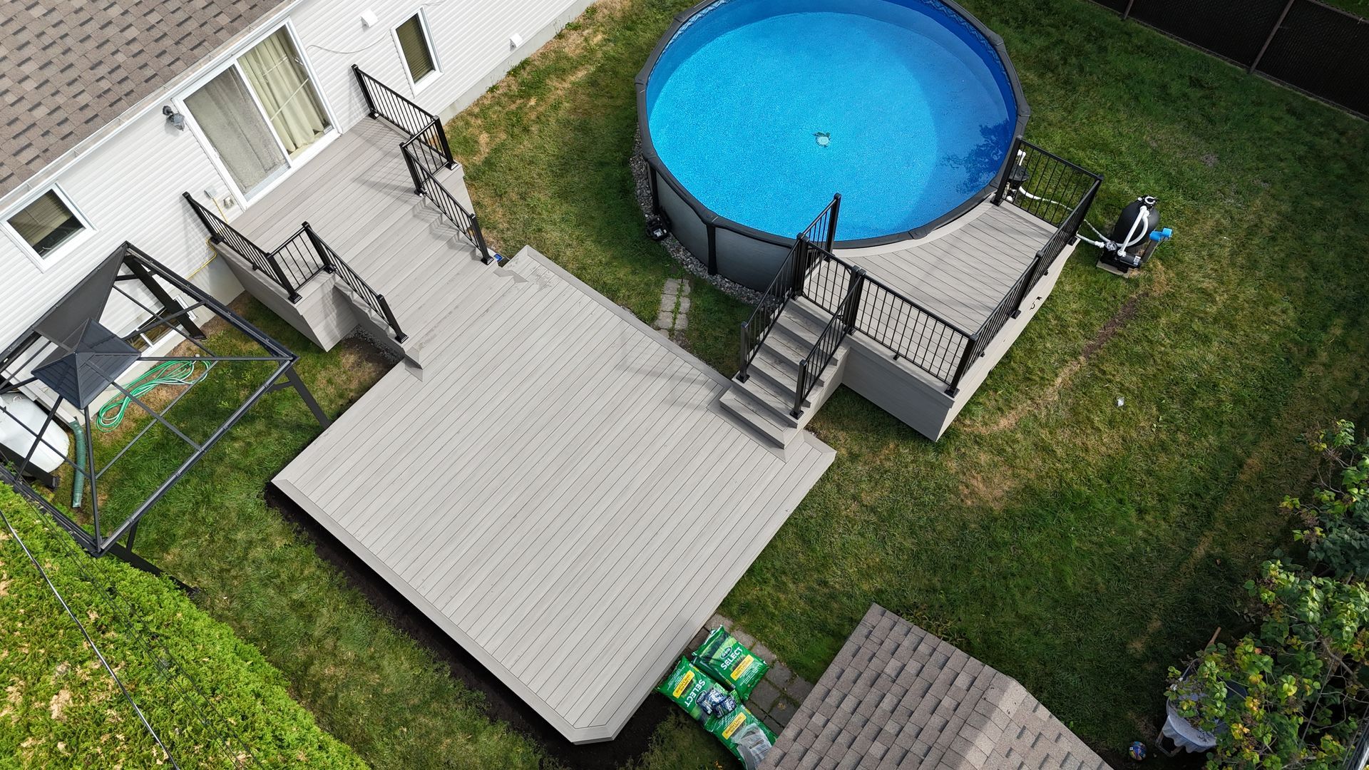 Terrasse arrière avec escalier, mobilier de jardin et piscine hors sol ronde à côté d'une pelouse.