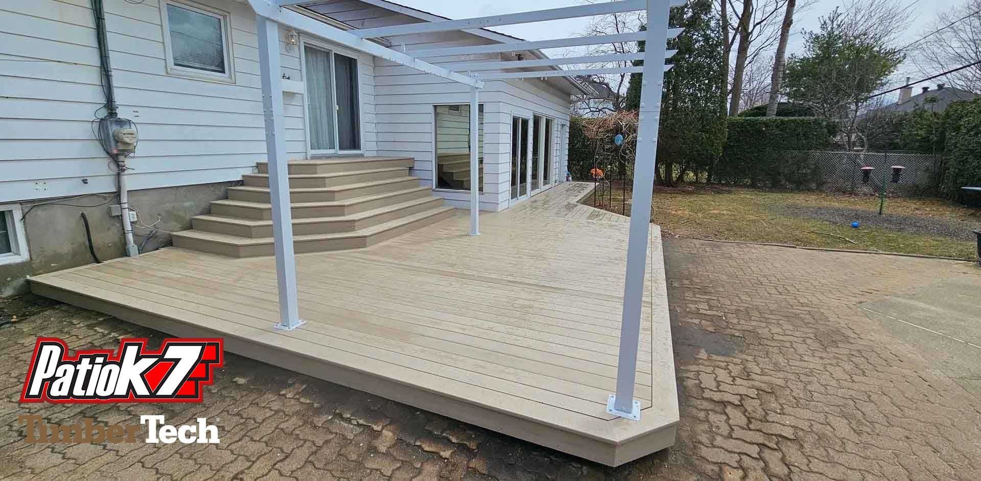 Terrasse en construction dans le jardin, avec poteaux et escaliers blancs, à côté d'une maison.