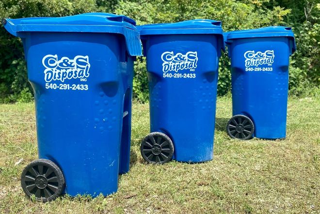 Three blue trash cans with lids and wheels on grass. C&S Disposal logo visible.