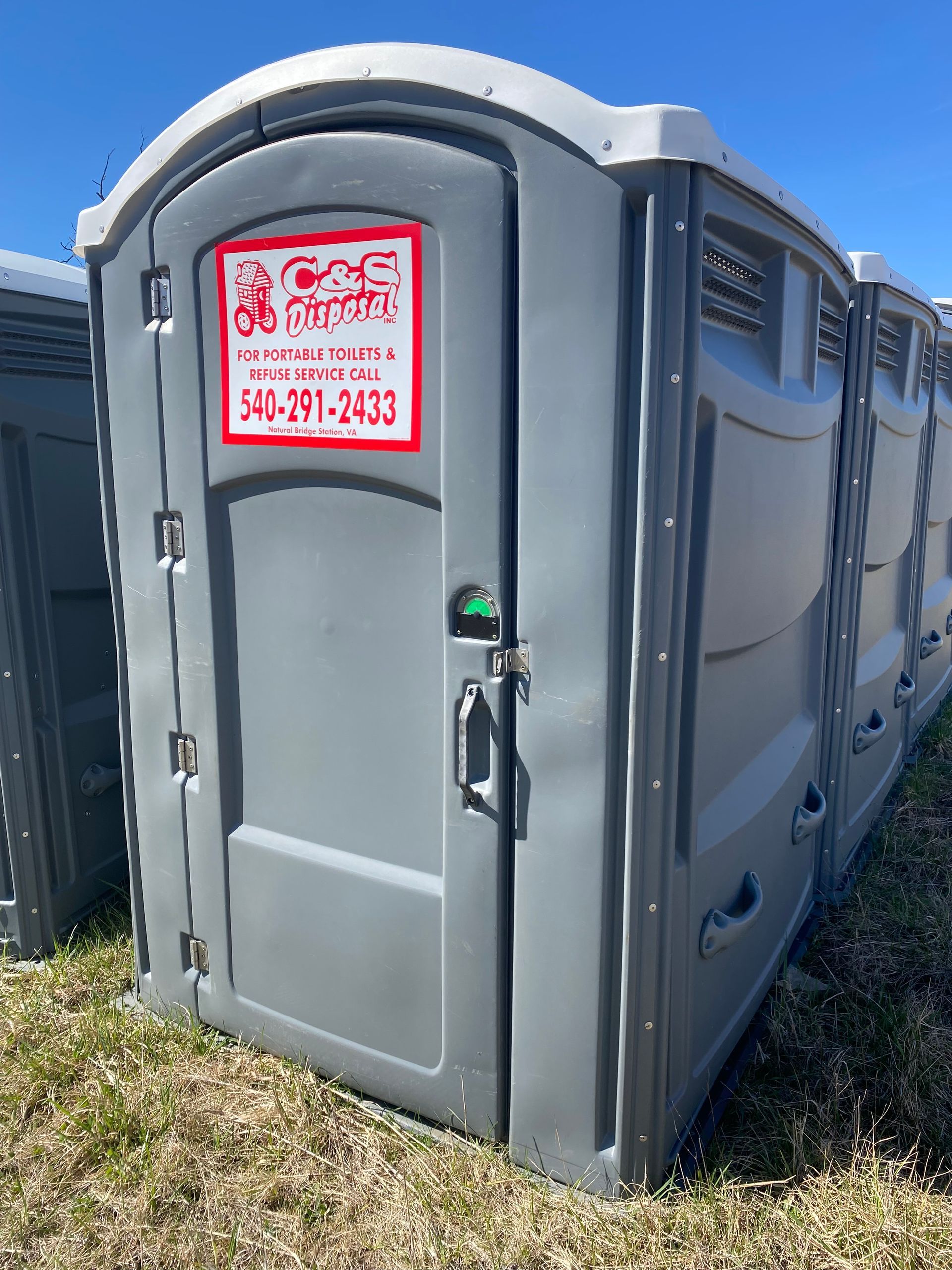 Gray portable toilet with white top and red logo, lined up outdoors.