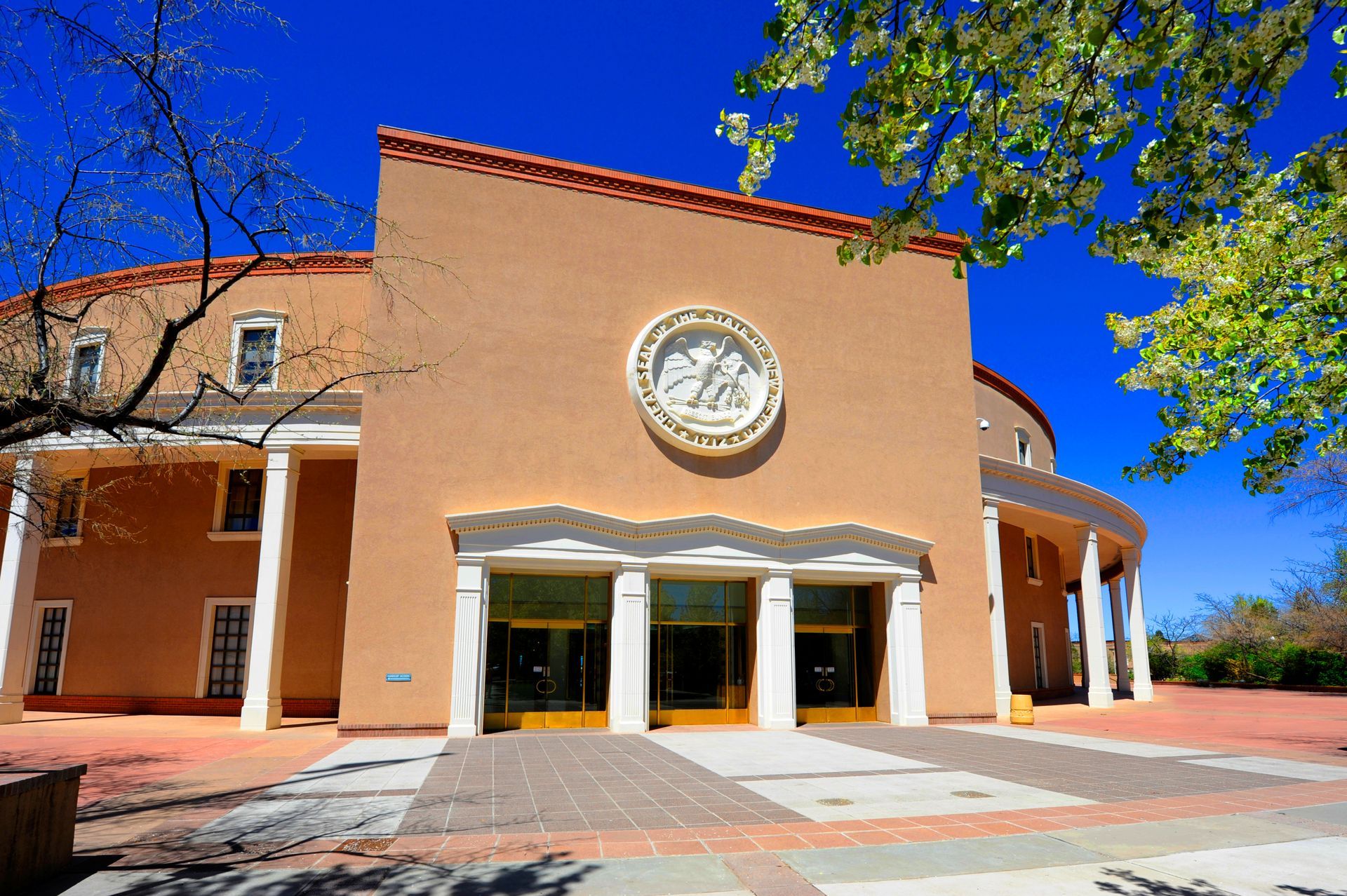 Desert adobe house with tan stucco walls, wooden fence, and shrubs under a blue sky Peach-colored building with columns and a clock emblem, under a bright blue sky