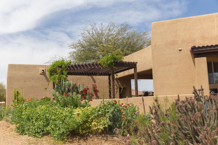 Desert-style adobe buildings with a shaded patio and green shrubs under a cloudy sky. Desert-style adobe buildings with a shaded patio and green shrubs under a cloudy sky.