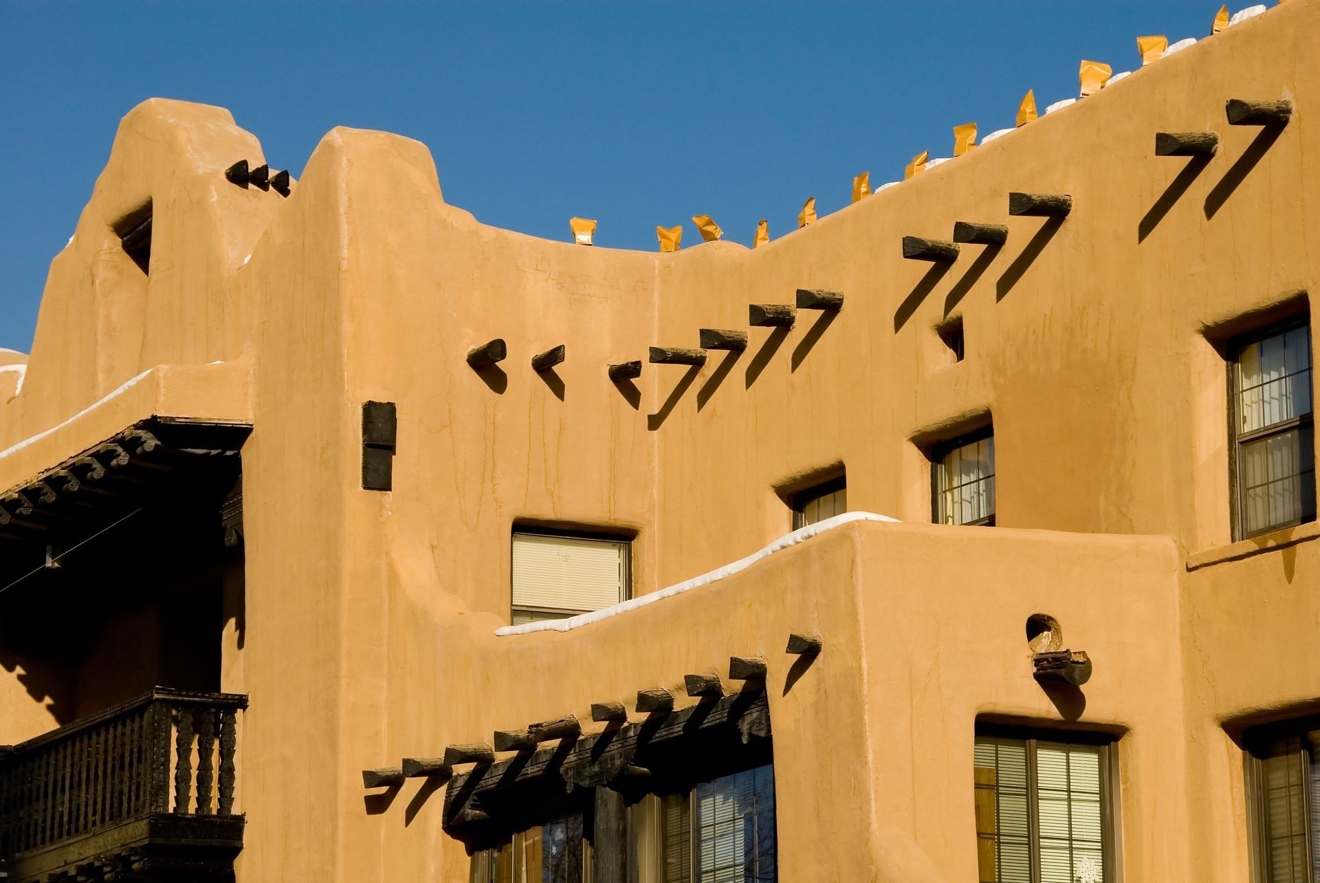 Sunlit adobe-style building with tan walls and dark geometric decorative accents under a blue sky Sunlit adobe-style building with tan walls and dark geometric decorative accents under a blue sky