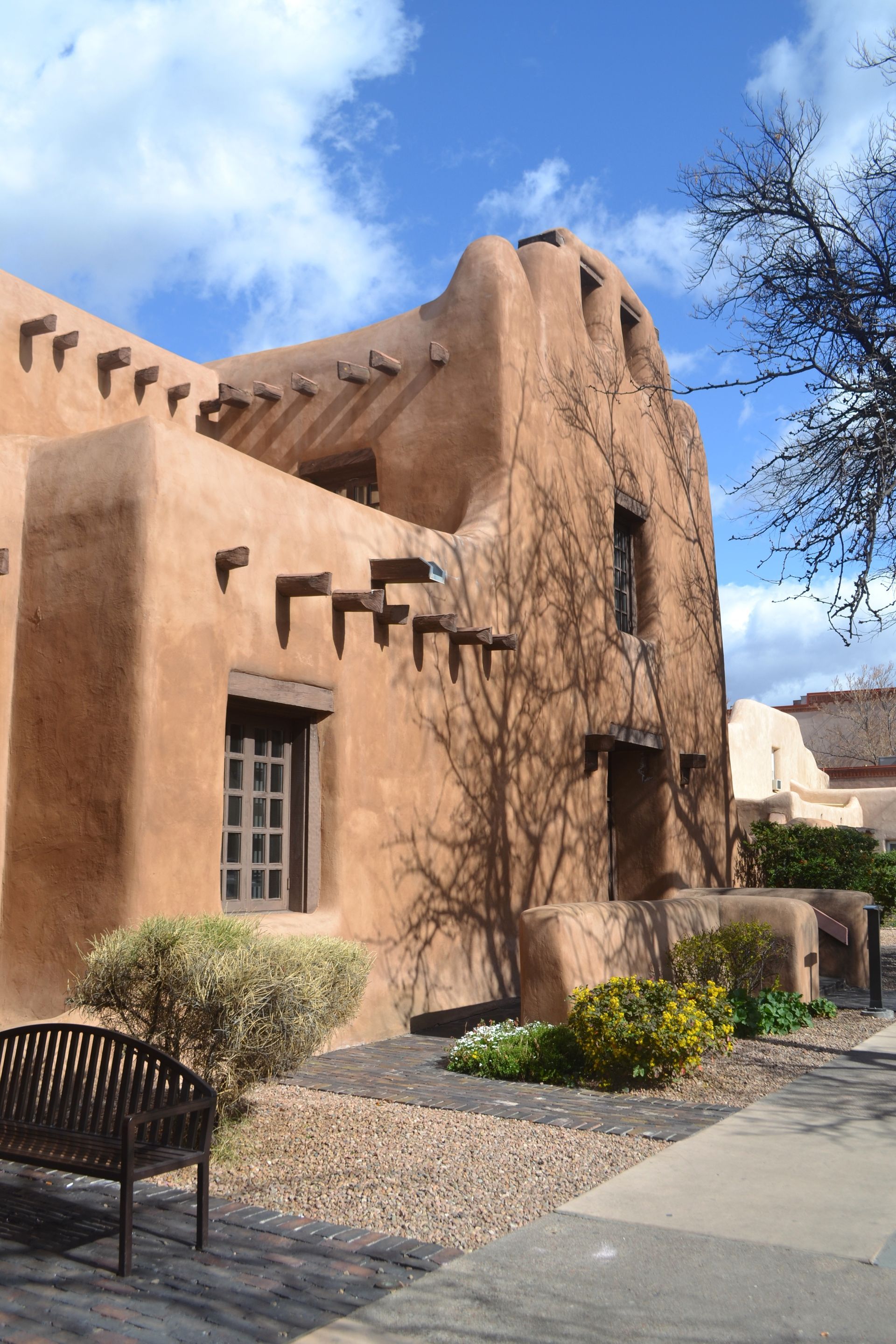 Adobe-style building with tan stucco walls, small windows, and a walkway under a blue sky Adobe-style building with tan stucco walls, small windows, and a walkway under a blue sky