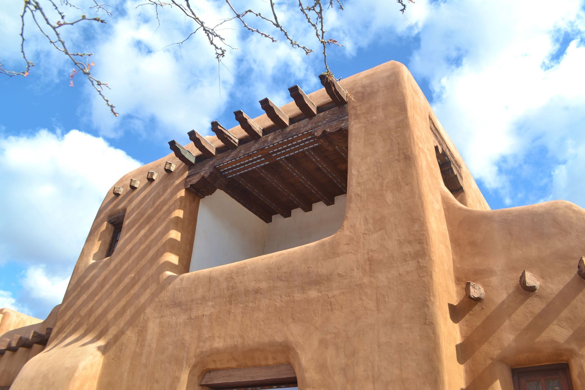 Adobe-style stucco building with wooden beams against a bright blue sky Adobe-style stucco building with wooden beams against a bright blue sky