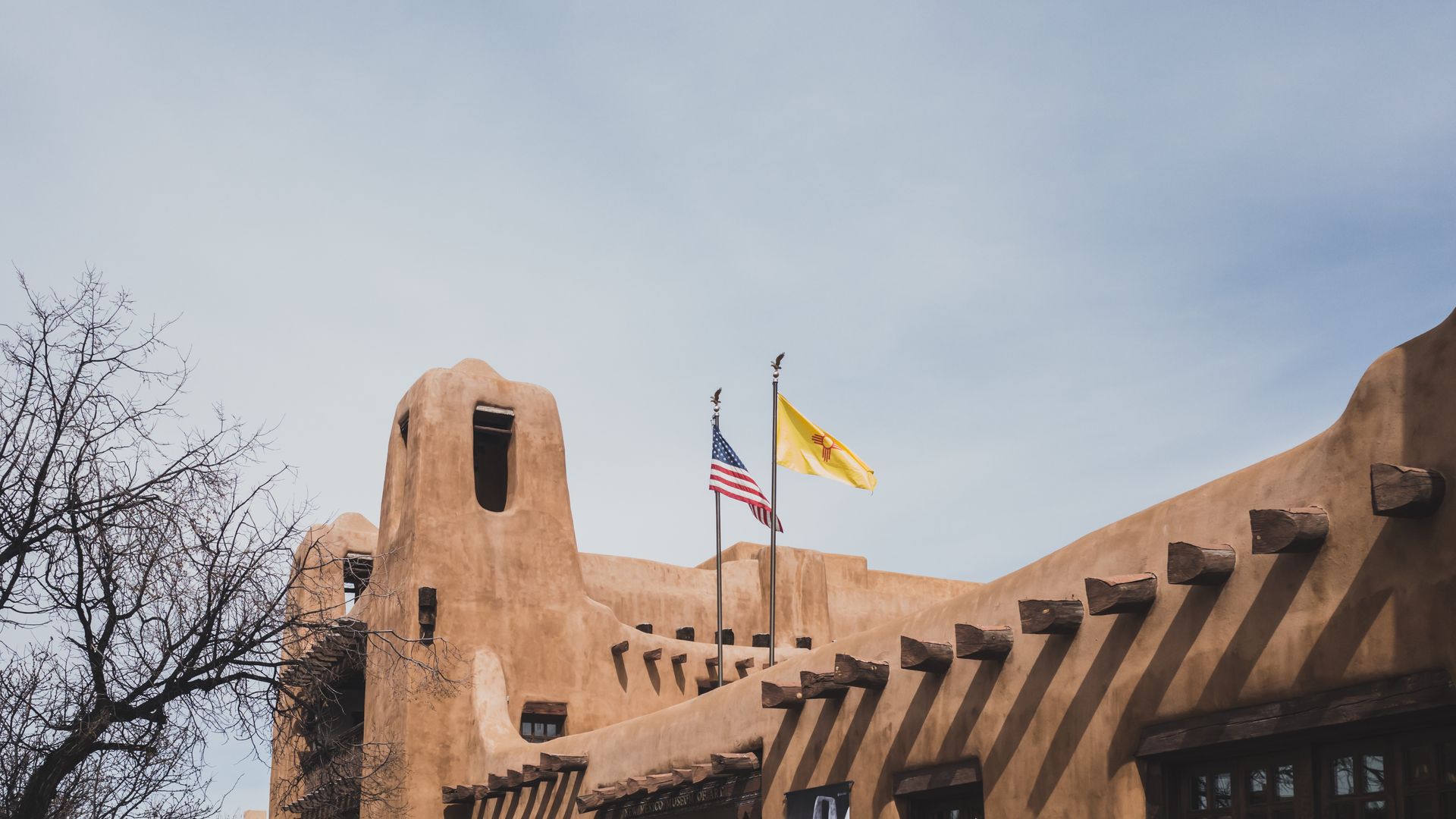 Adobe-style building with three flags on poles against a cloudy sky