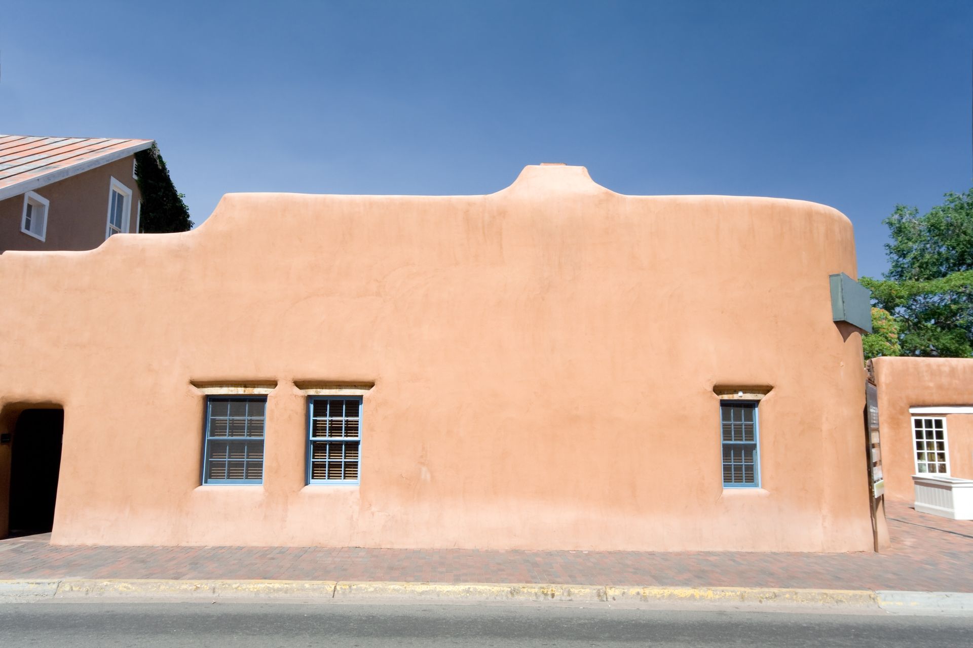 Adobe-style stucco building with peach walls, small windows, and a flat roof under a blue sky