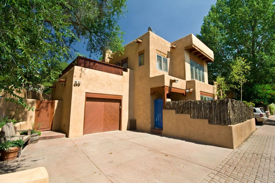 Tan house with a garage, blue door, and fenced patio on a sunny tree-lined street Tan house with a garage, blue door, and fenced patio on a sunny tree-lined street