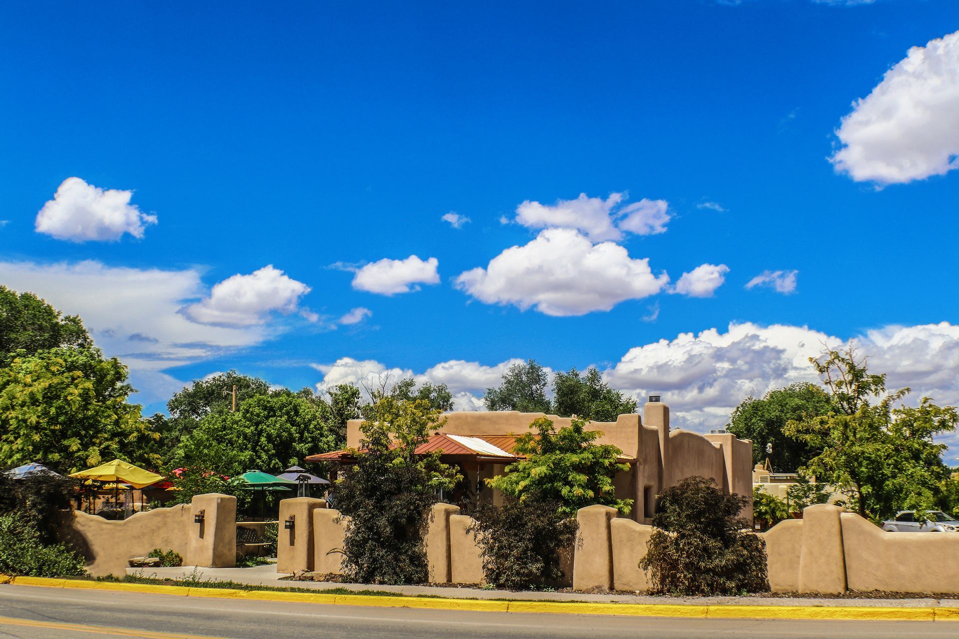 Adobe-style stucco house behind a wall under a bright blue sky with fluffy clouds