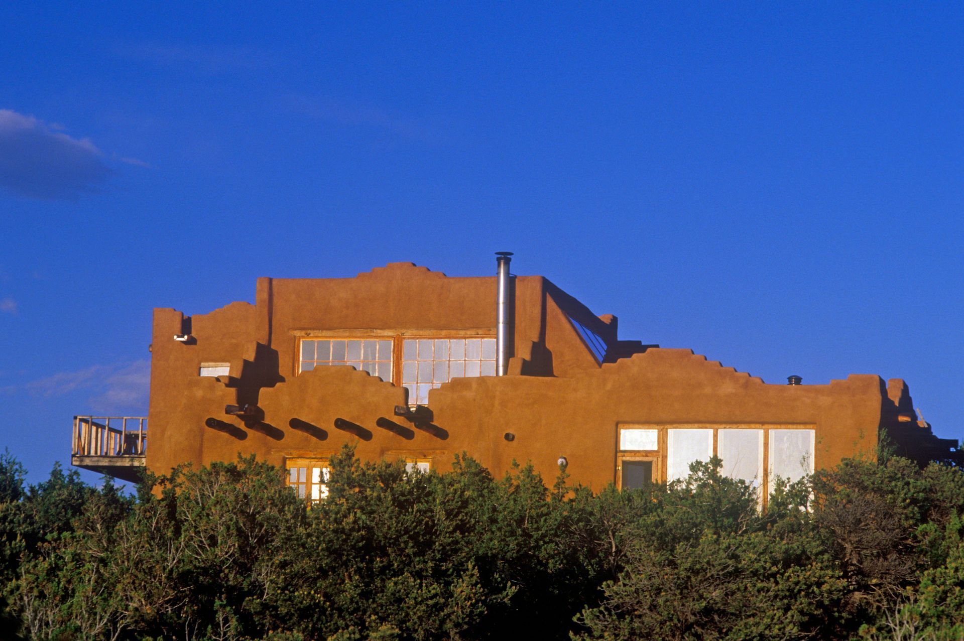 Adobe-style orange house behind green bushes under a clear blue sky