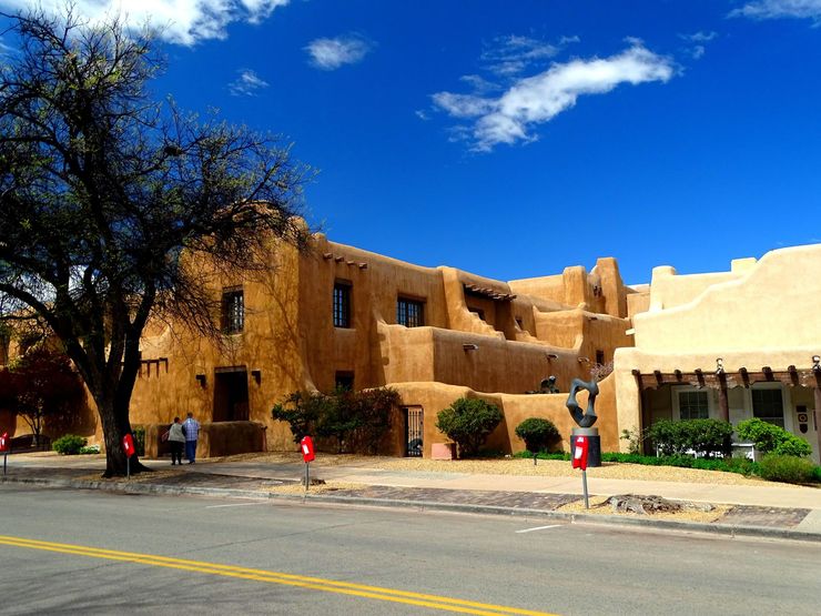 Adobe-style building under a bright blue sky, with a tree and road in the foreground. Adobe-style building under a bright blue sky, with a tree and road in the foreground.