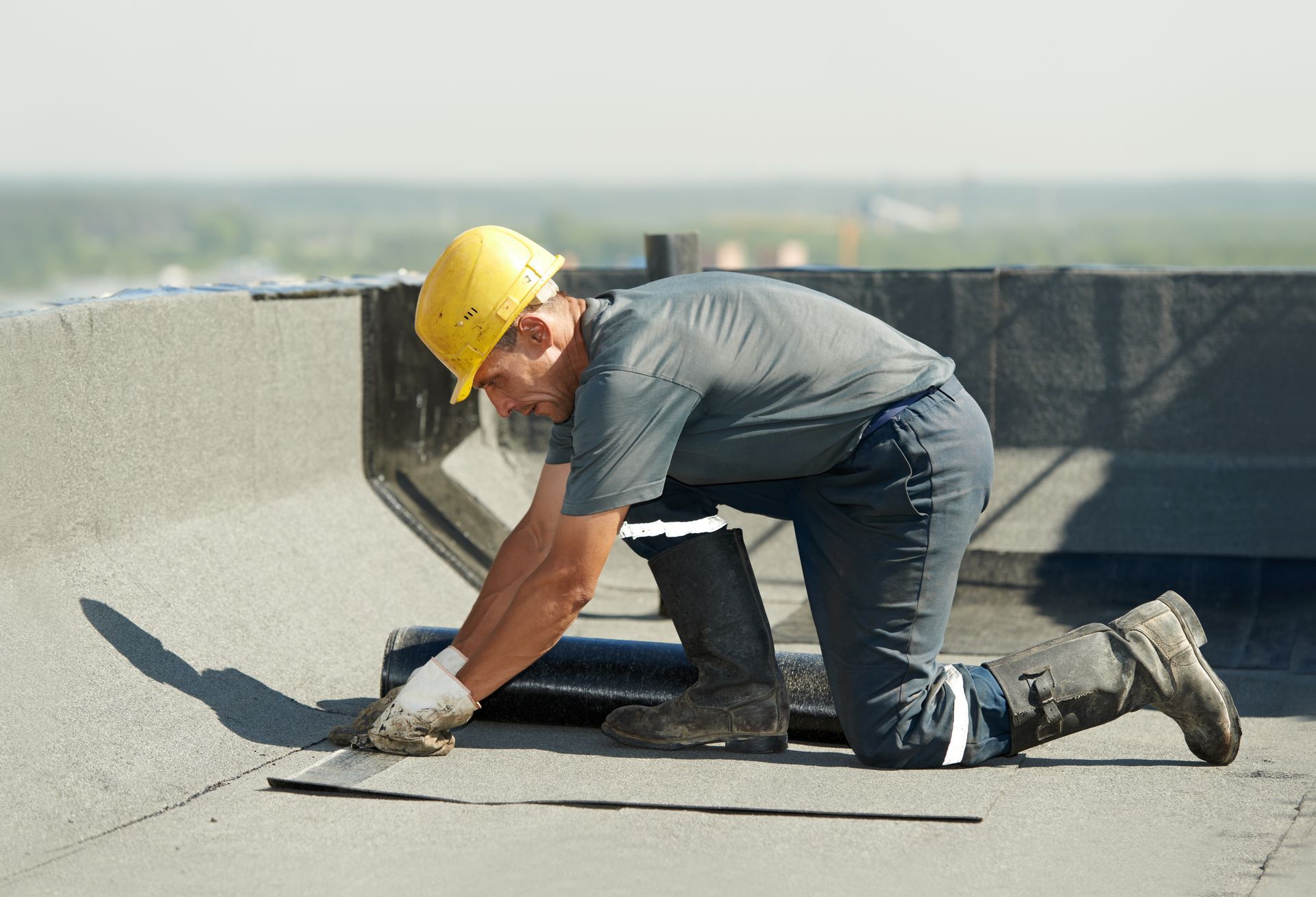 Construction worker in yellow hard hat kneeling on a rooftop, smoothing concrete with a trowel.